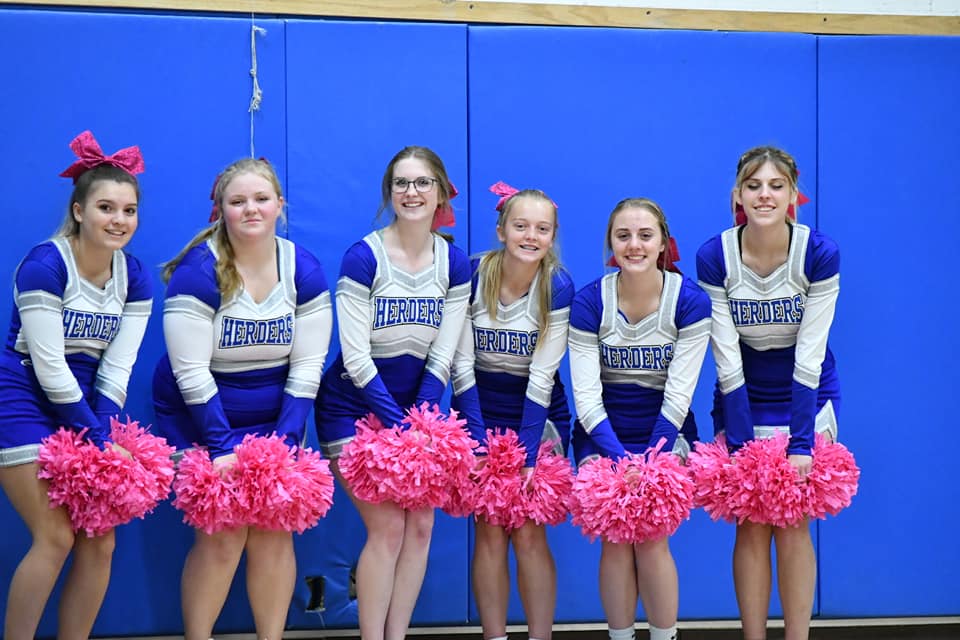 5 cheerleaders line up and pose with pink pom poms at a home game