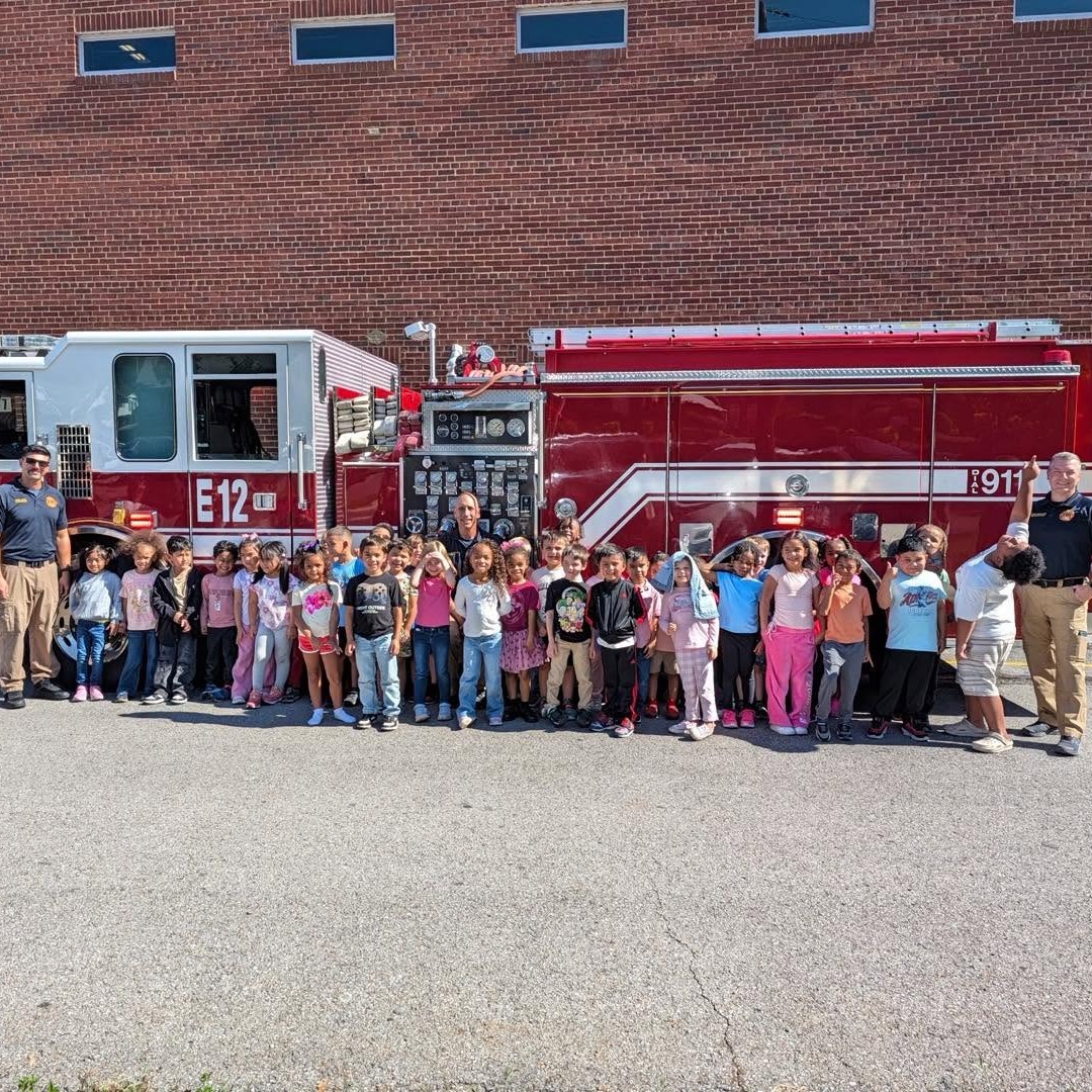 A group of children and two adults stand in front of a red fire truck.