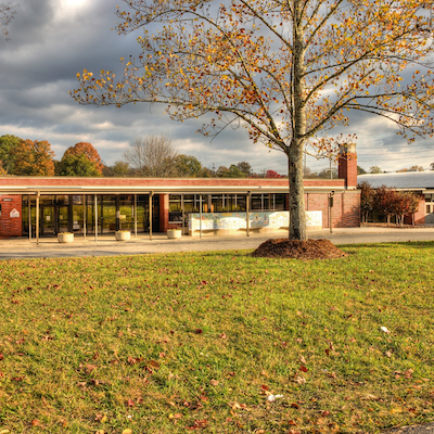 Exterior of a red brick building with glass windows and a flagpole, set against a cloudy sky.