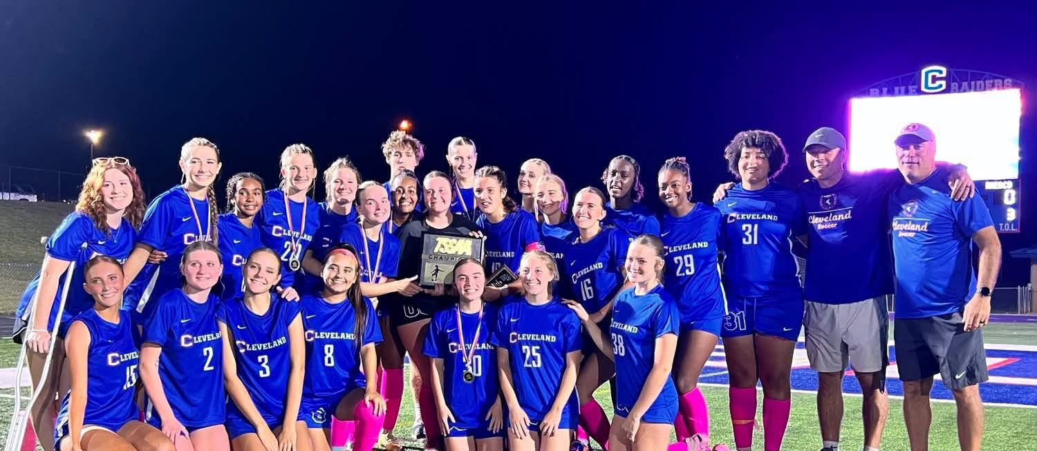 A team of young girls and adults in blue jerseys pose for a photo on a field.