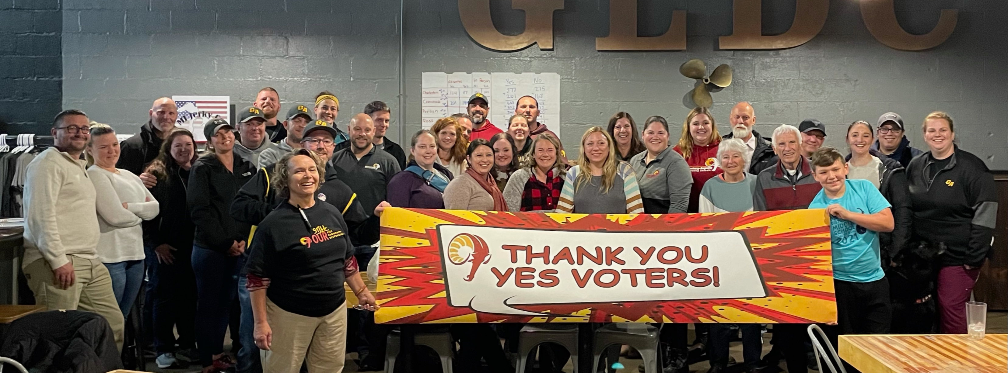 Ms. Somers and a group of GACS staff and community members are smiling and holding a banner that says Thank You Yes Voters! 