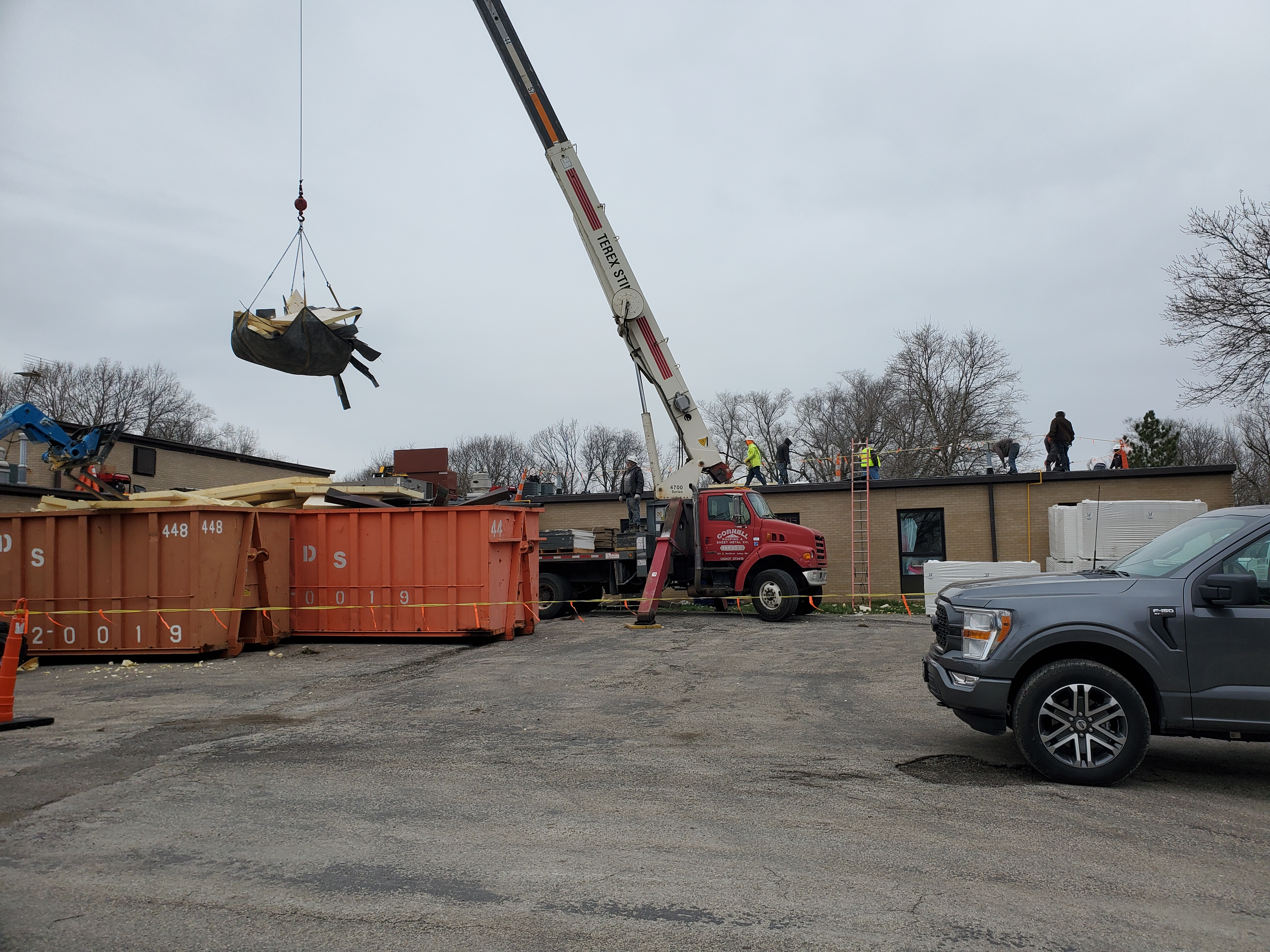 orange dumpsters in front of amazonia elementary school. a large crane lifts heavy roofing materials onto the roof 