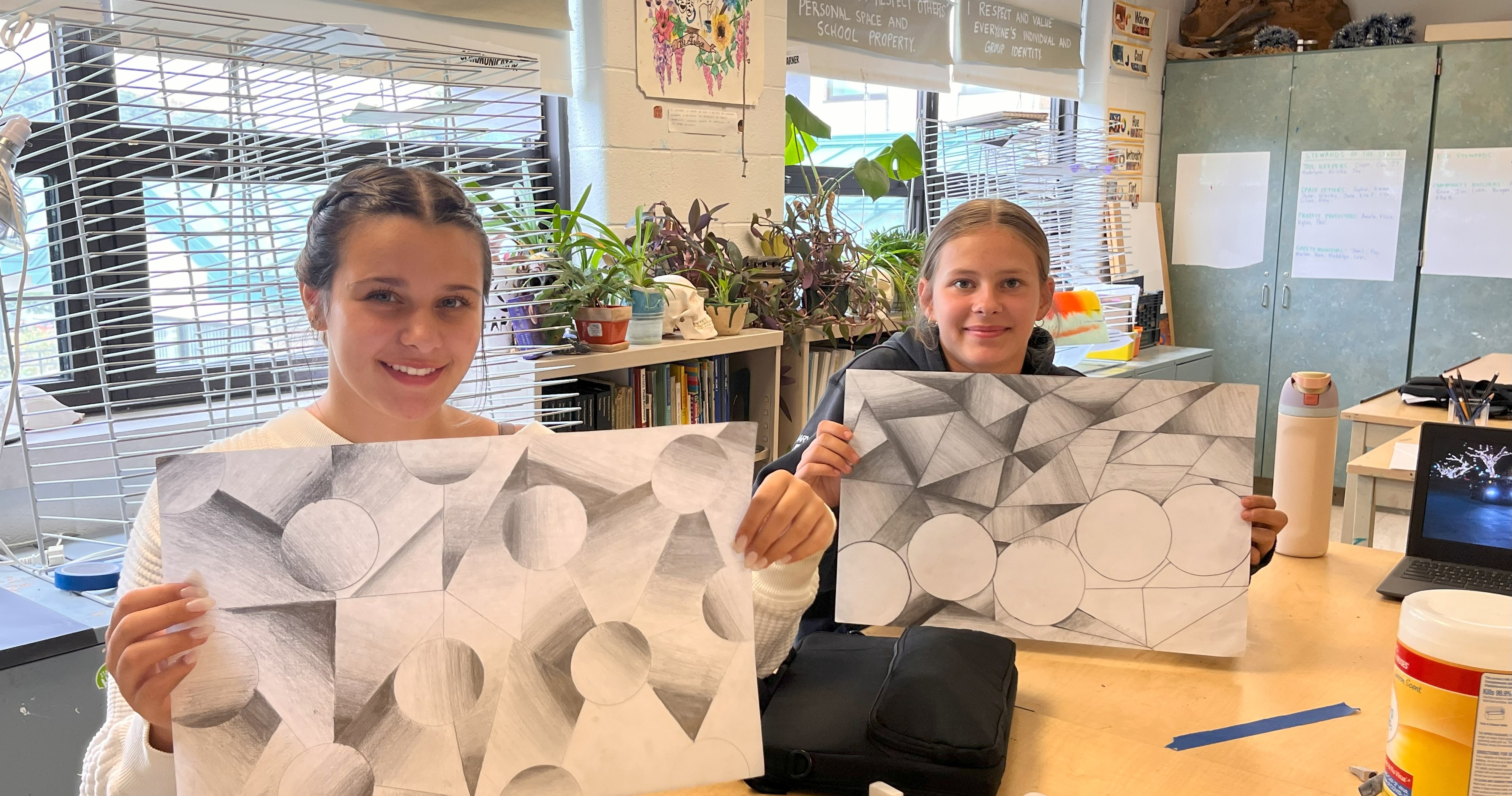 Students in art class pose with their graphite drawings that demonstrate their knowledge of shading and value