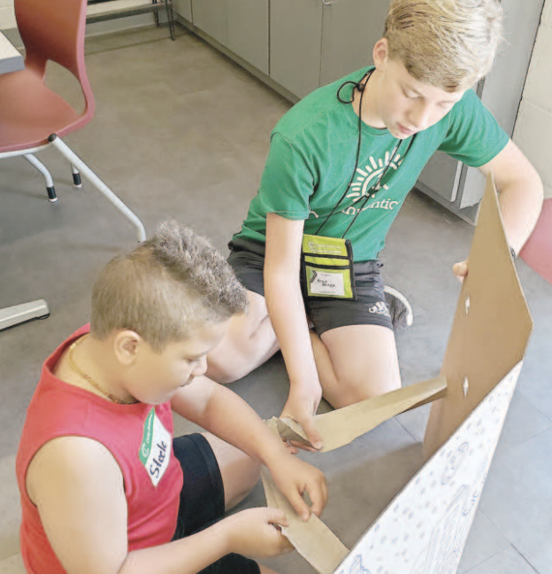 A student volunteer helps a camper complete his marble arcade.