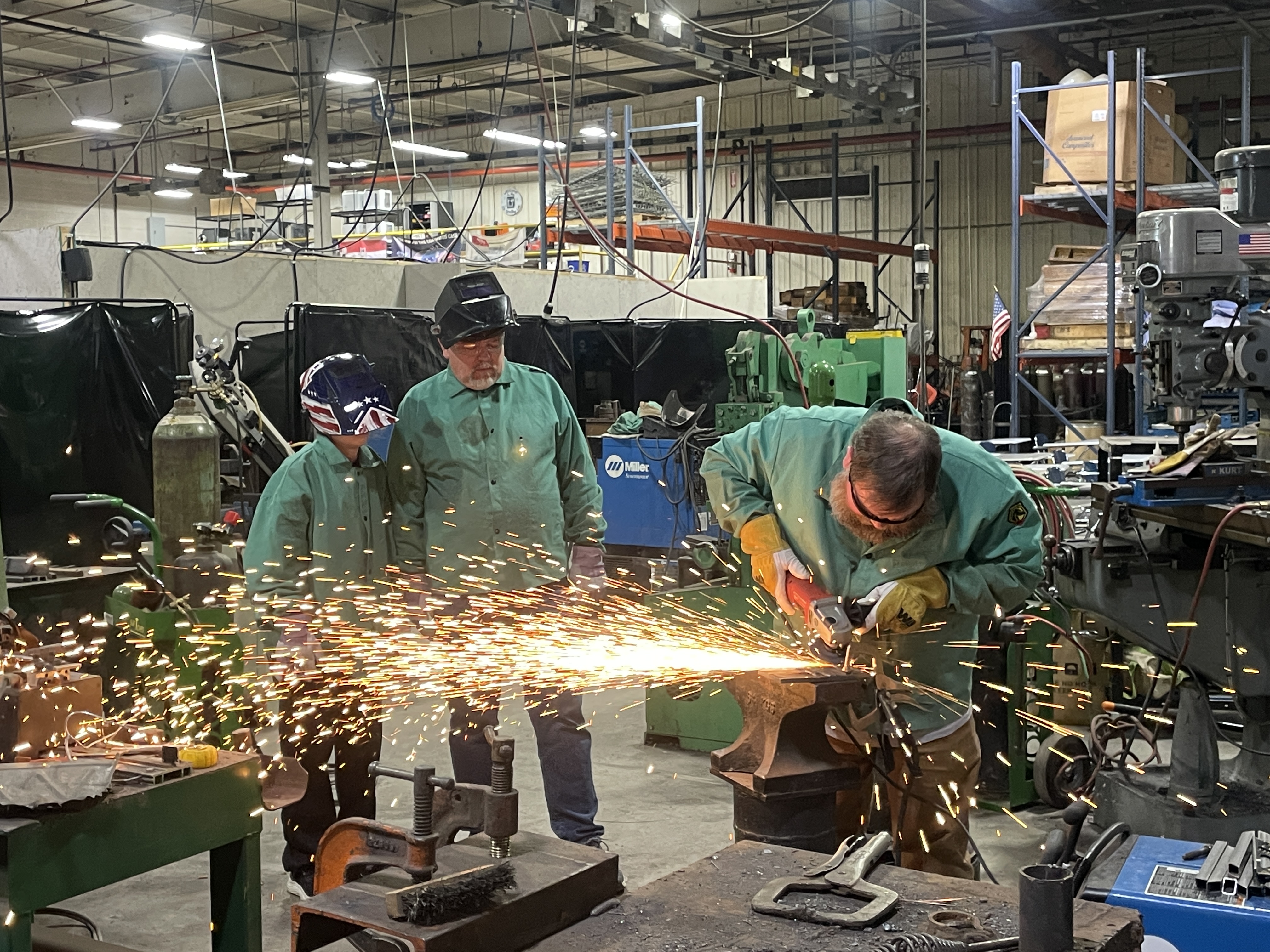 three people at a welding project, one welding with sparks flying