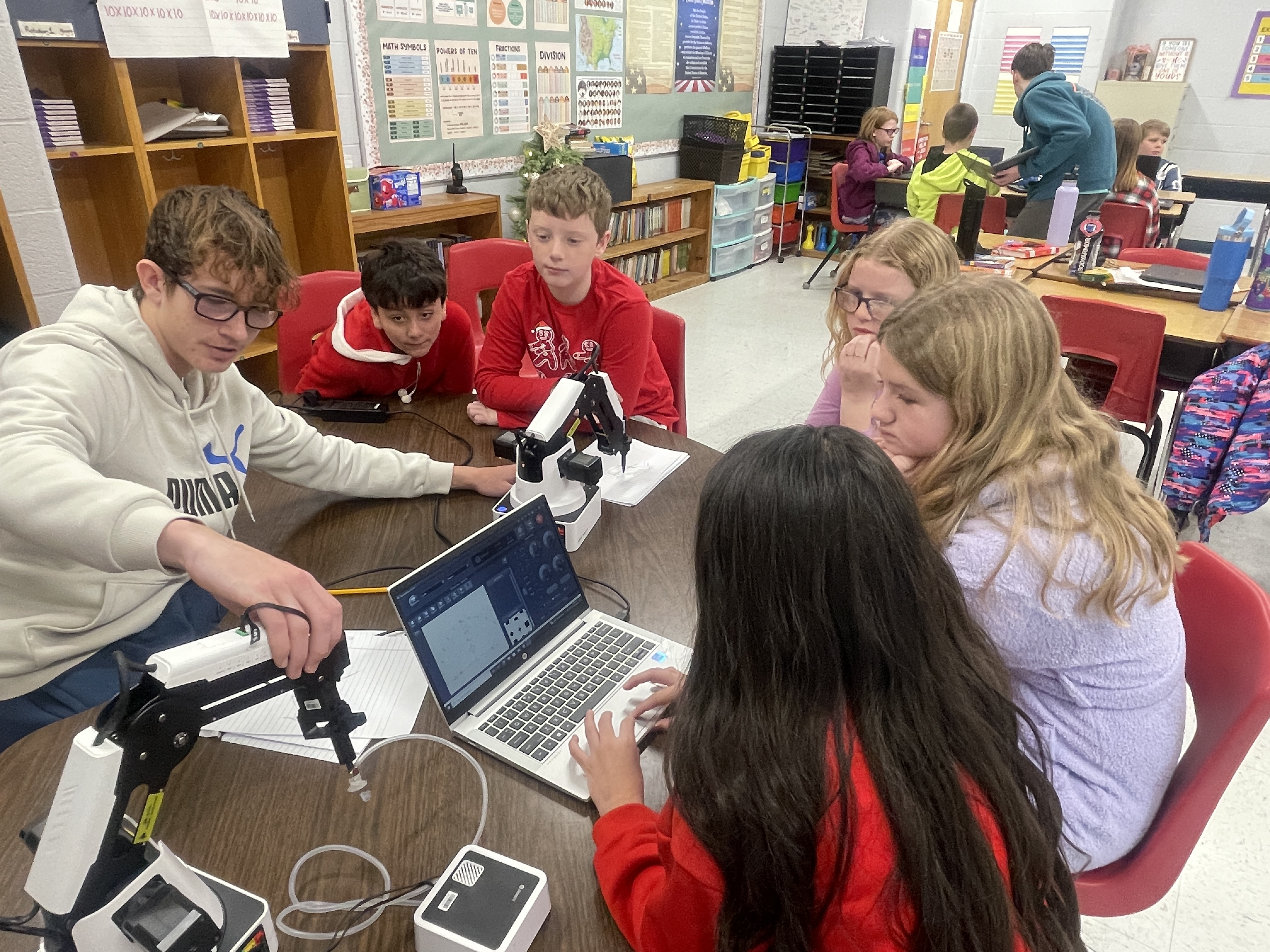 young studnets at a table with a robotic arm and laptop