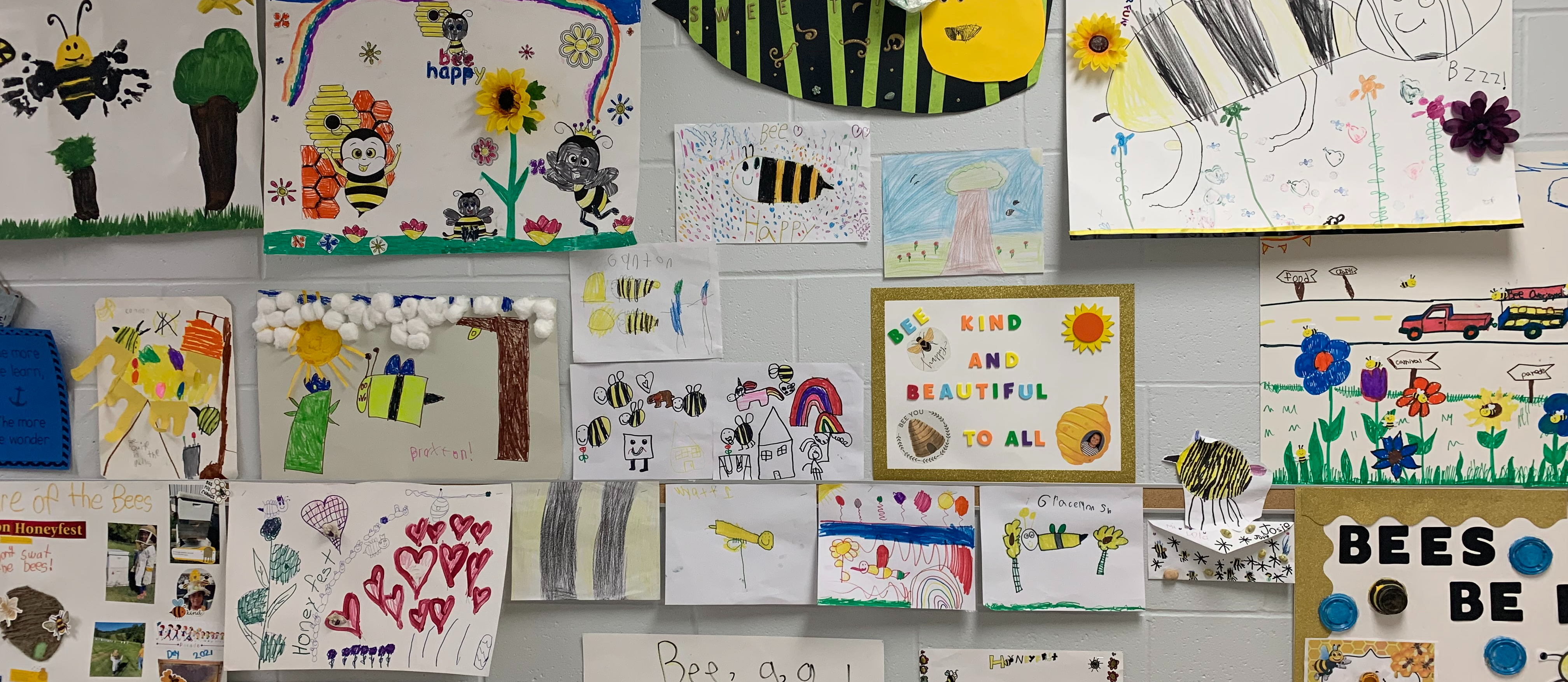 Honeyfest Poster Contest - student made posters featuring bees, trees, flowers and other honey-themed drawings on a white school wall