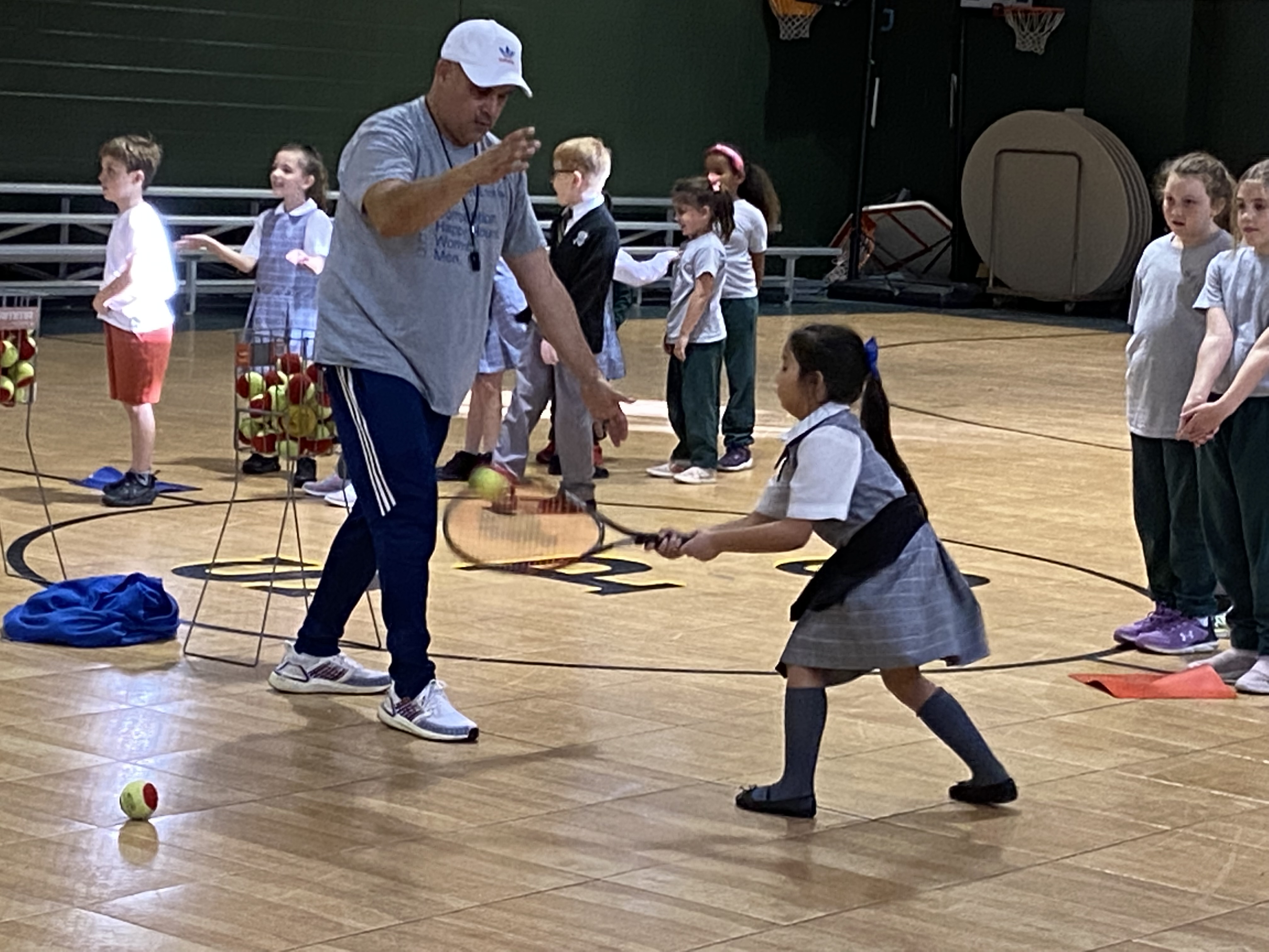 a student hits a tennis ball while her coach looks on