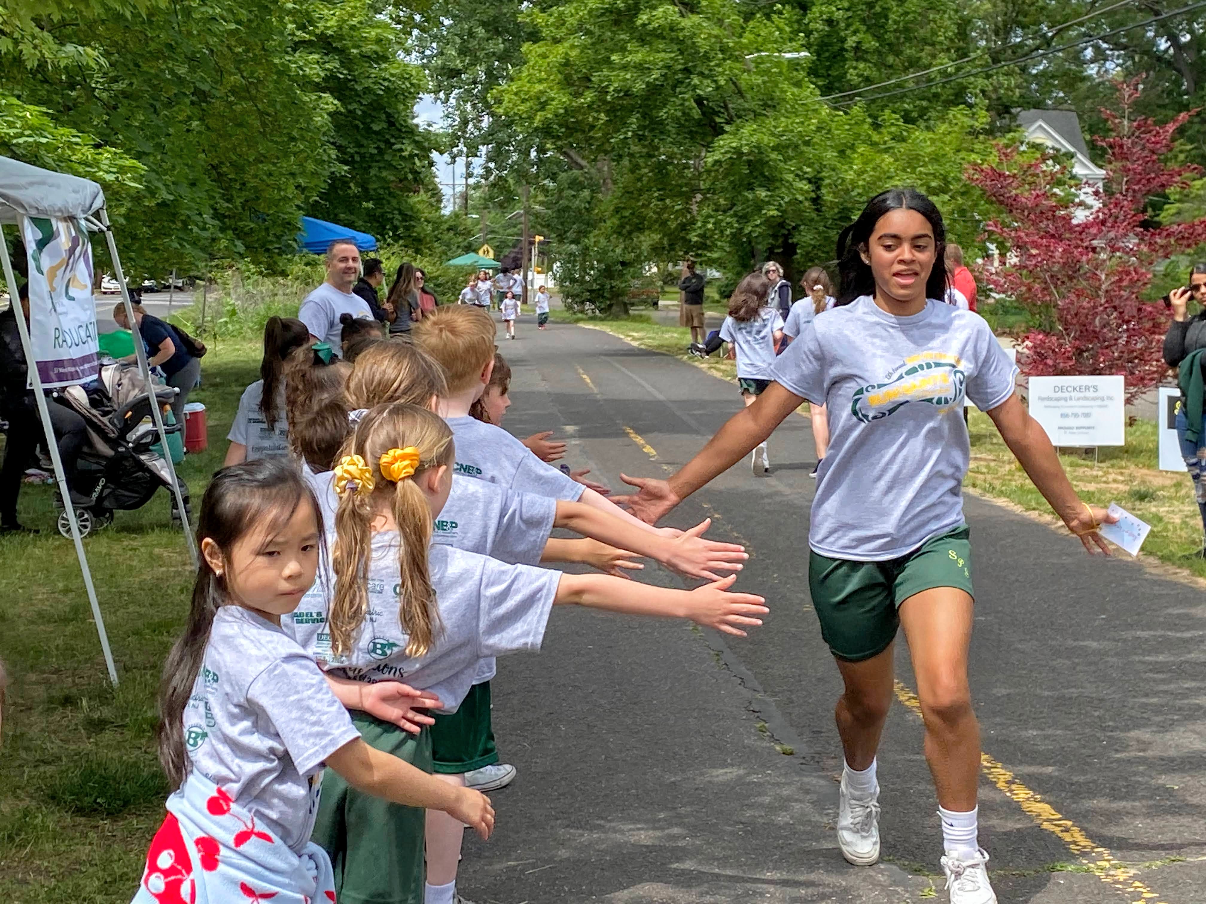 a group of 2nd grade students high-fiving a 7th grade student as she runs past 