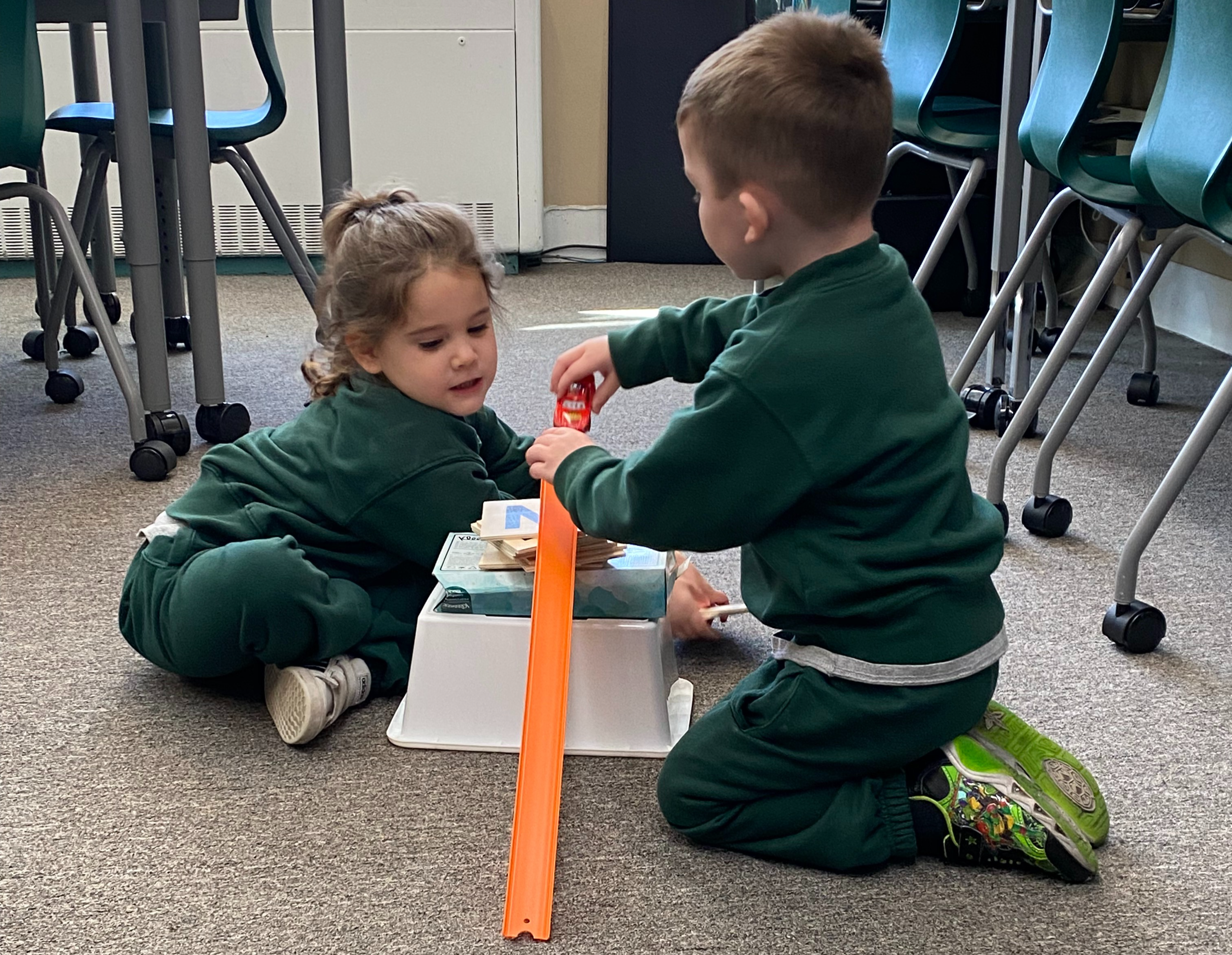 A preschool girl and boy working together to build a ramp for a miniature car