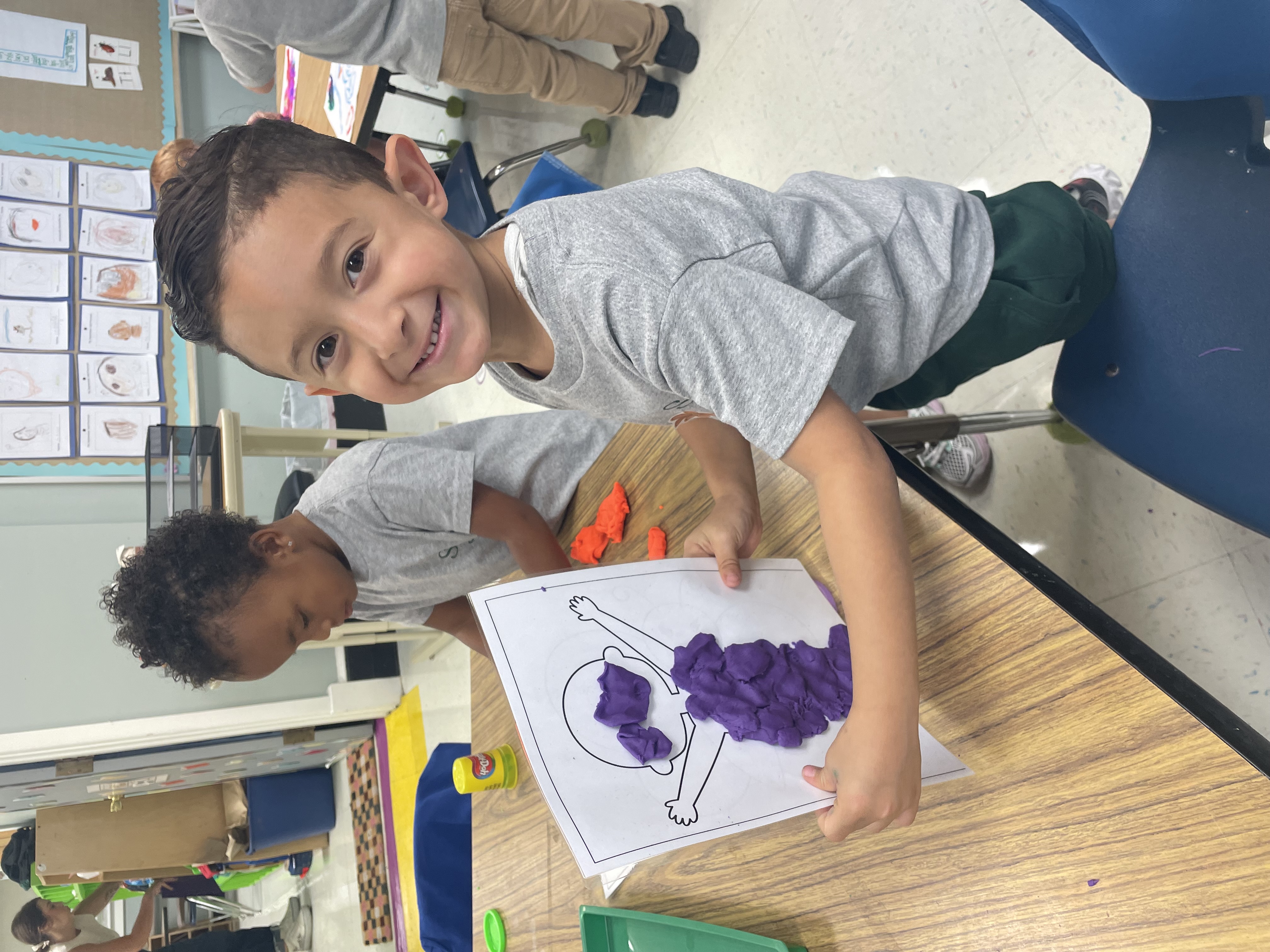 A preschool age boy holding up his artwork proudly