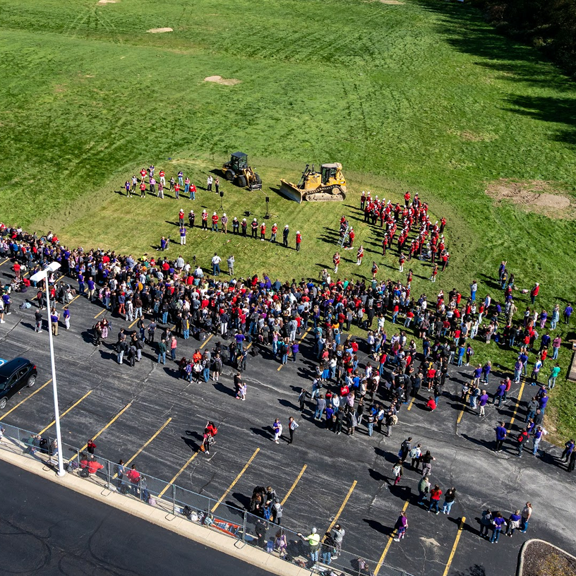 Aerial view of people gathered in a parking lot, with machinery vehicles and green grass.