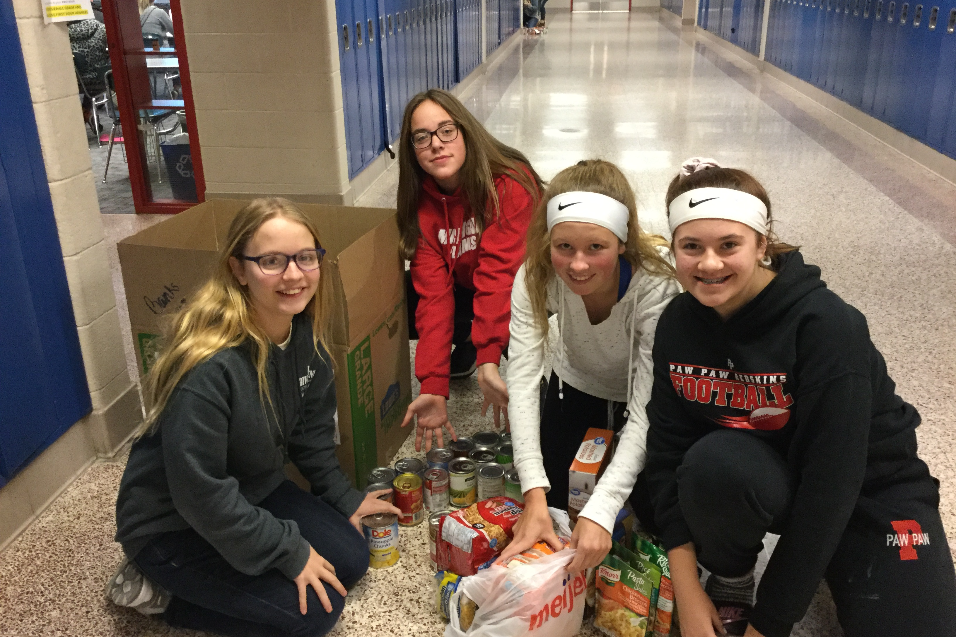 Students posing for a picture in the hallway working on a food drive.