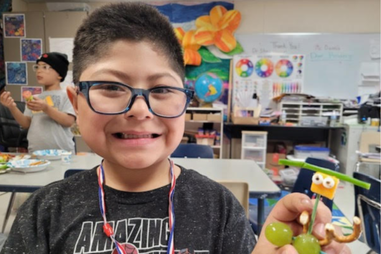 student showing off his grape, cheese, and toothpick sculpture