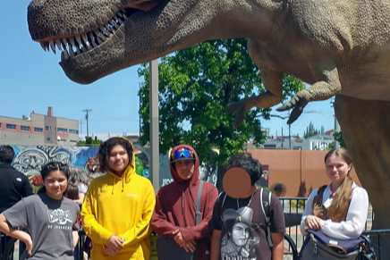 HMS A-List students and their teacher pose in front of the t-rex statue at OMSI