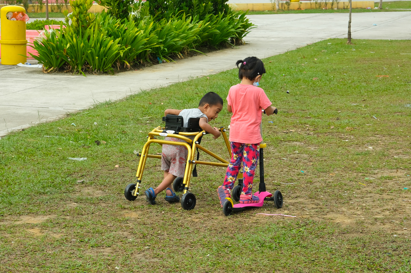 two kids one with a walker one on a scooter