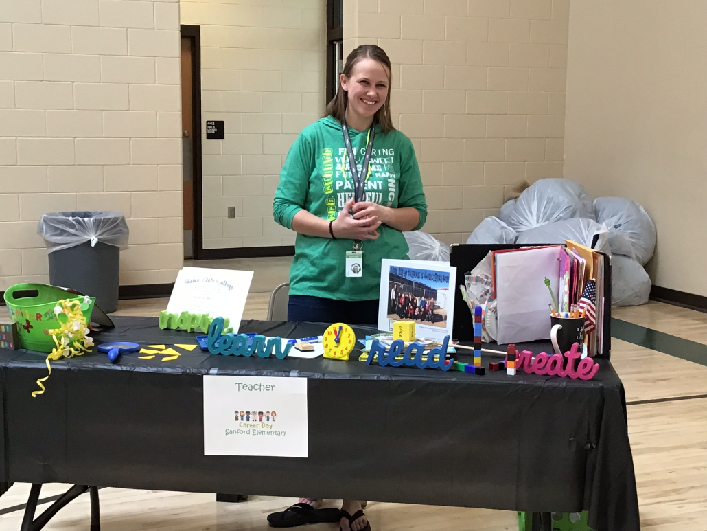 photo of a teacher standing behind a table