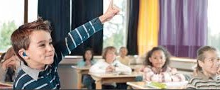 Young boy with hearing device raising his hand in class