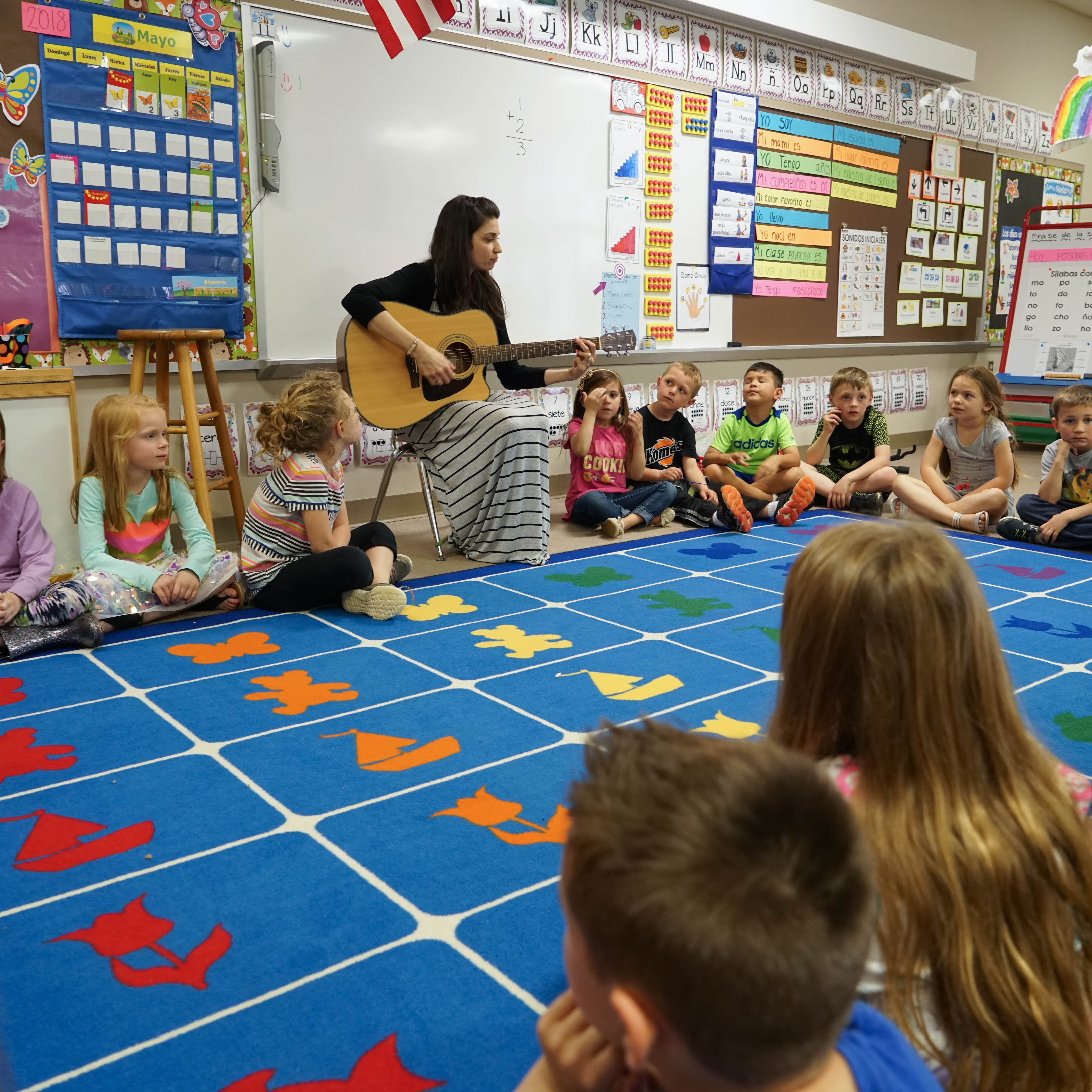 teacher playing guitar for students seated on floor