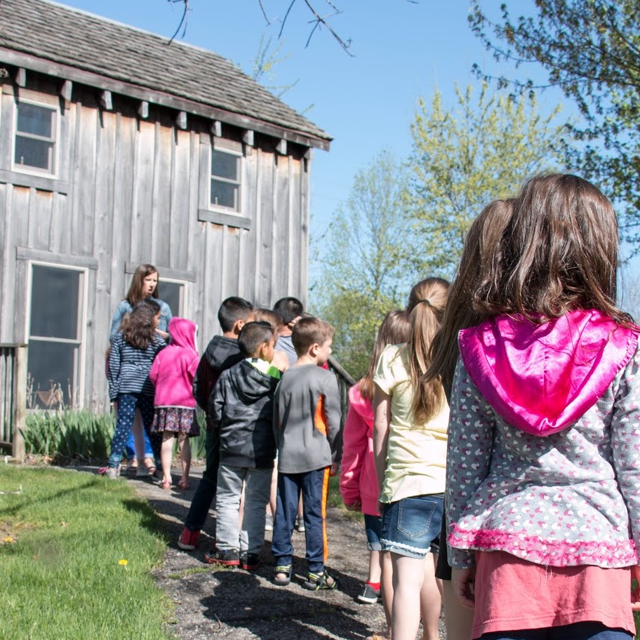 Students lined up outside of a historic wood building with their teacher leading 