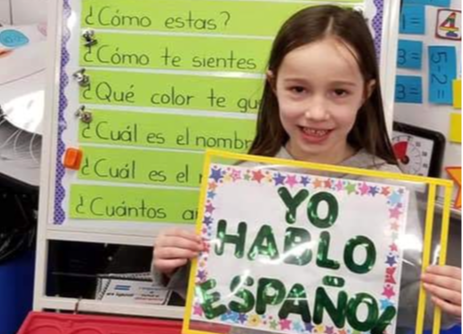 student smiles while holding "yo hablo espanol" sign