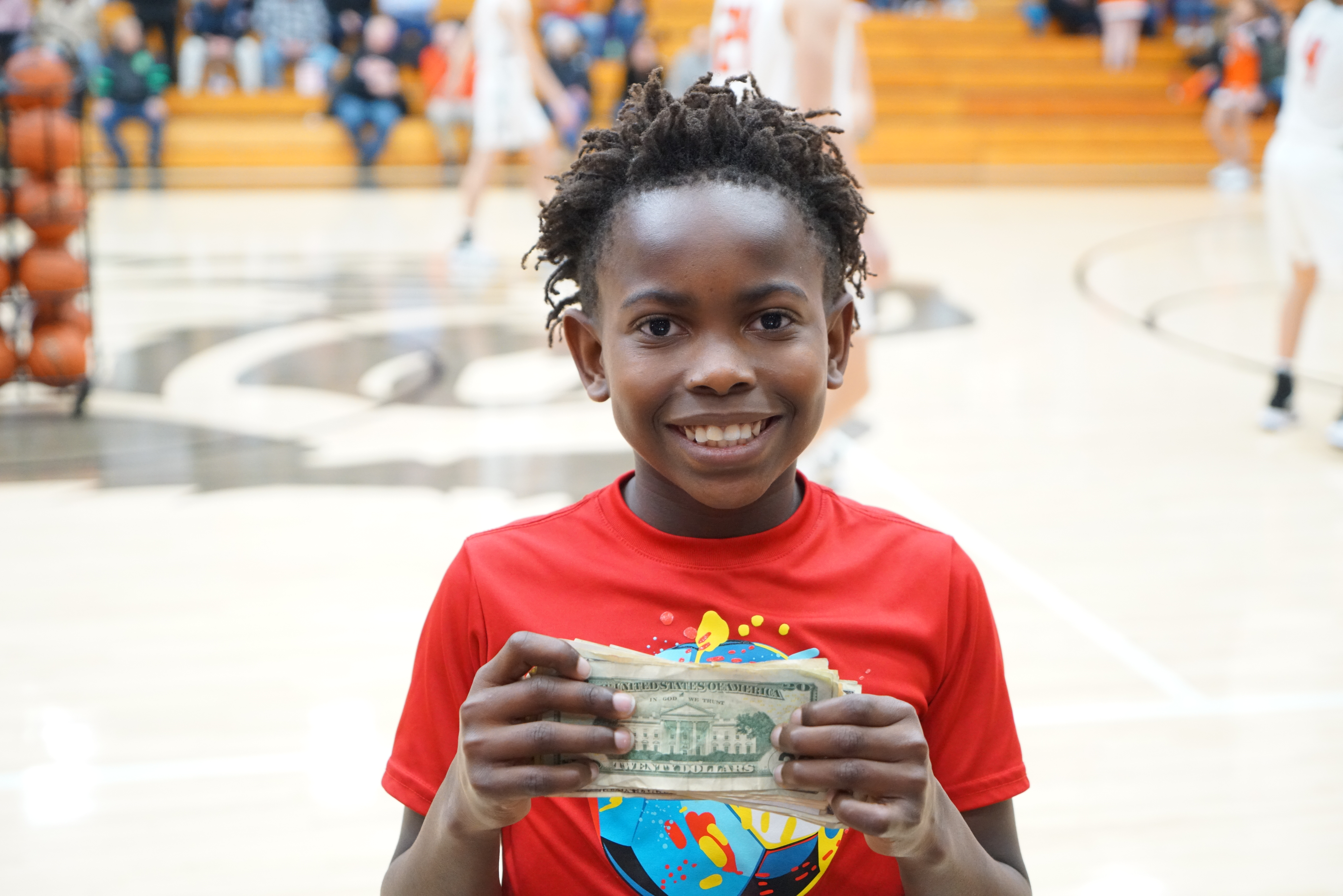 Student smiles on the basketball court while holding up 20 dollar bills