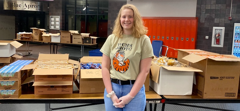 JROTC Volunteer smiles in front of food donation boxes