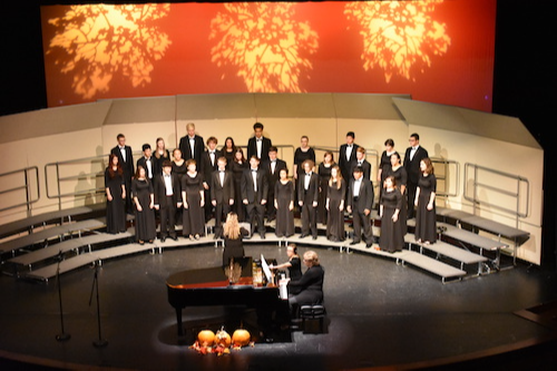 Vocal Music & Music Theory: Choir students stand in suits and gowns on stage with their conductor and accompanying pianists 