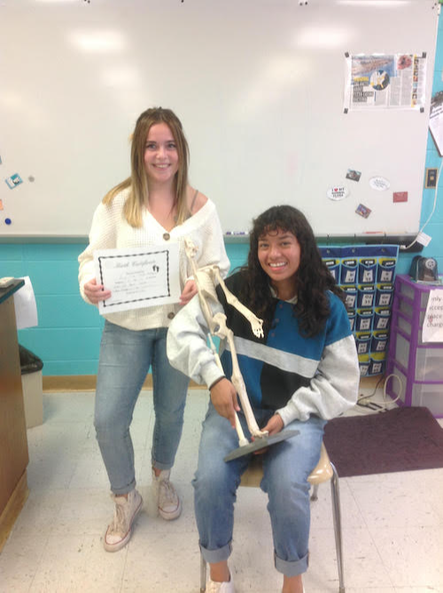 students pose with an anatomical model of a skeleton and an award