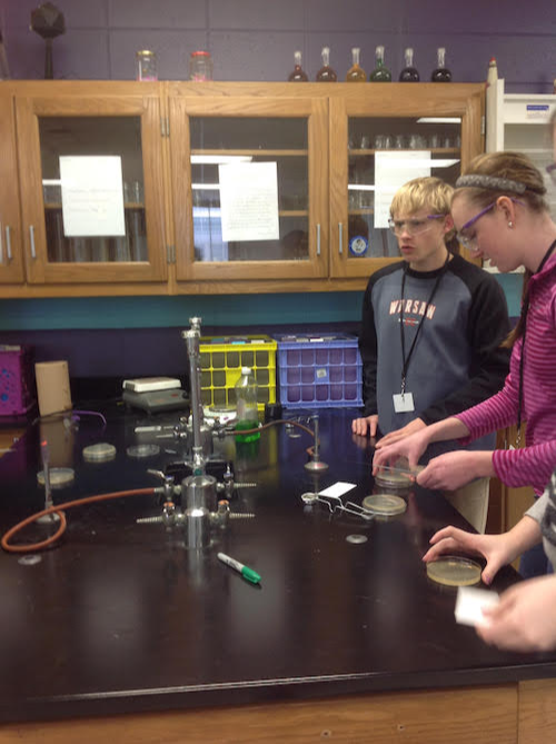 students prepare petri dishes next to a large bunsen burner