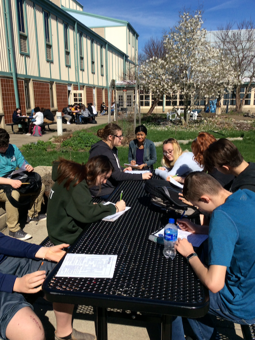 students sitting outside at a picnic table working on worksheets
