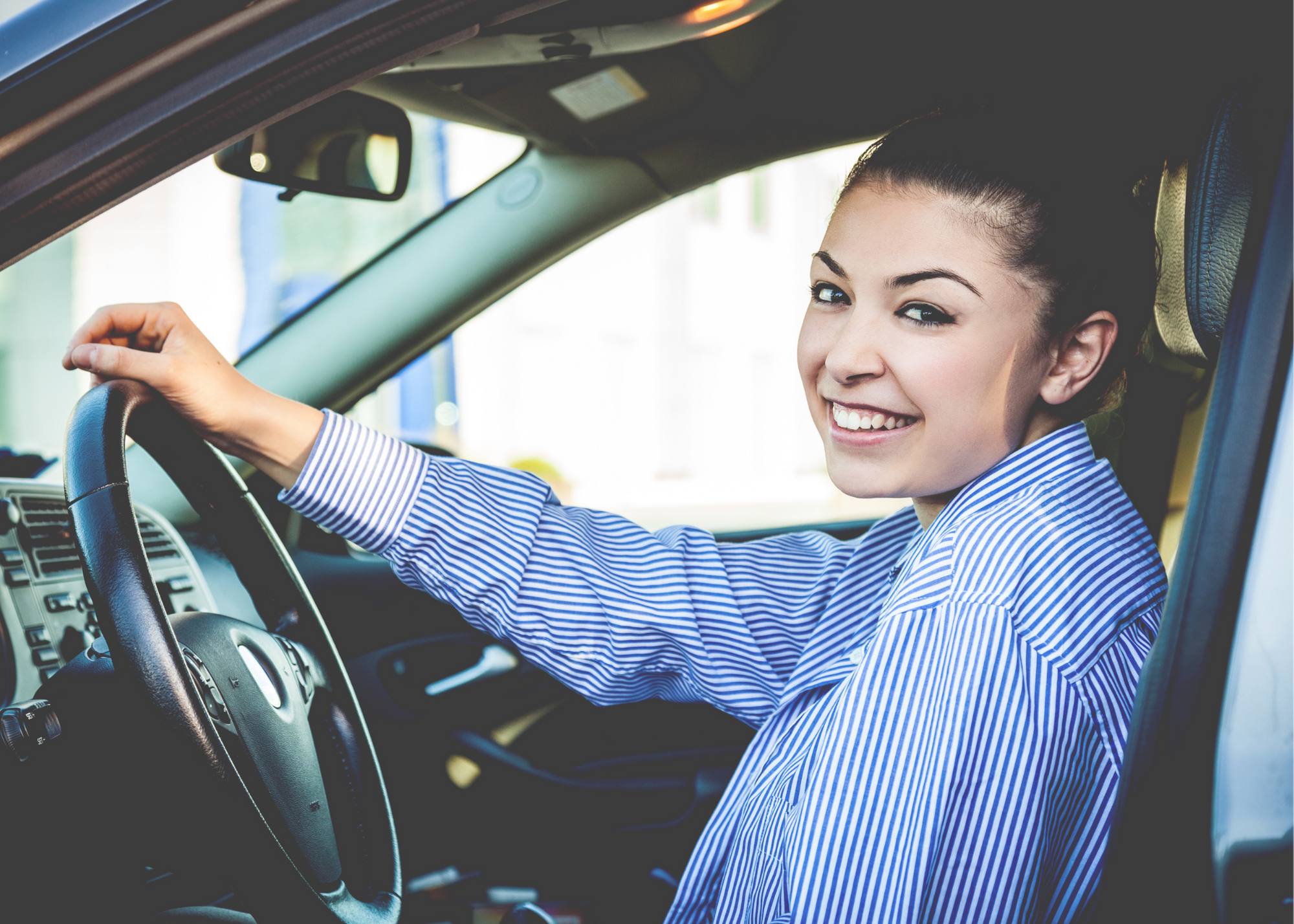 photo of young woman smiling in a car with one hand on the wheel