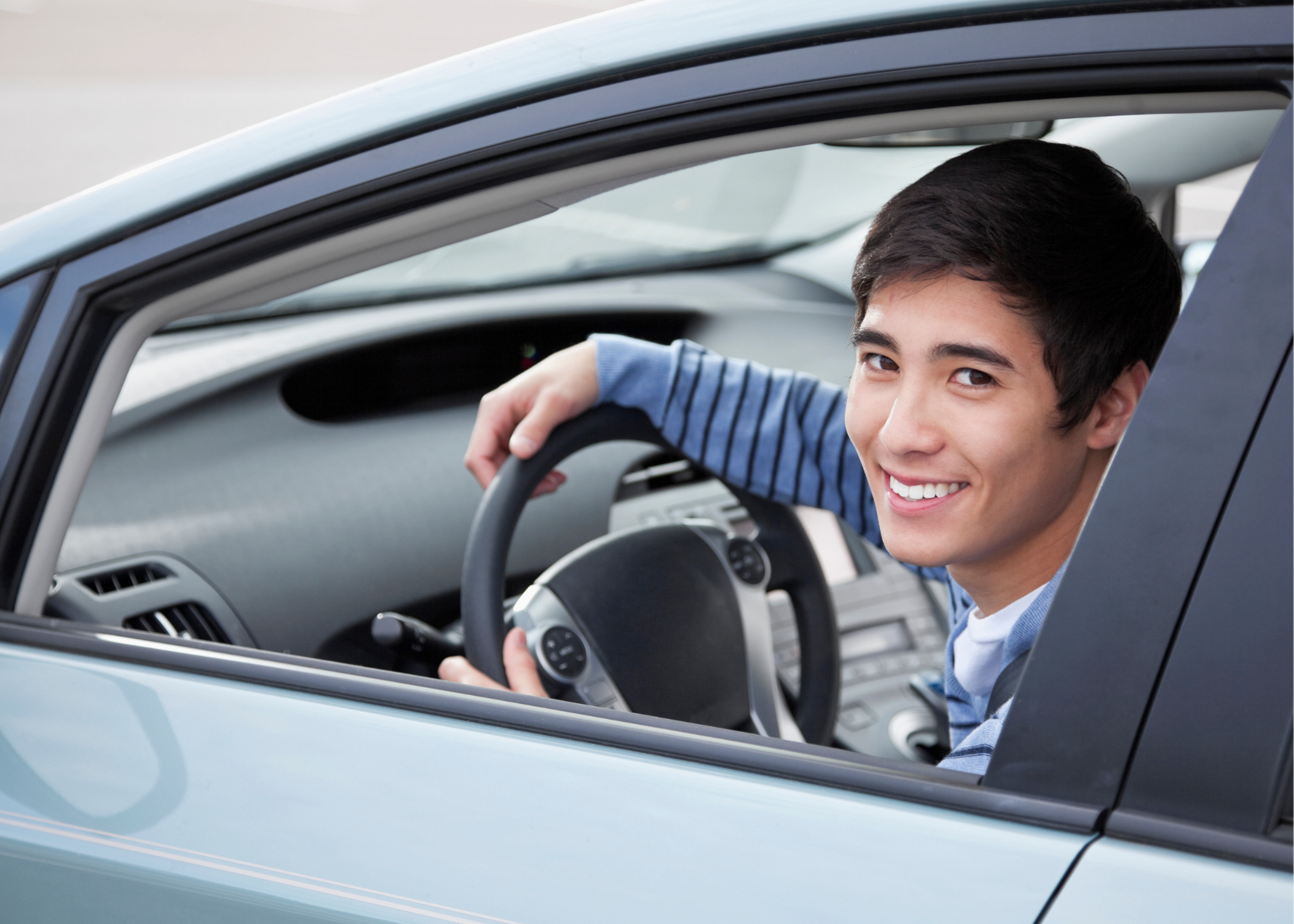 photo of young man smiling in a car with hands on the wheel