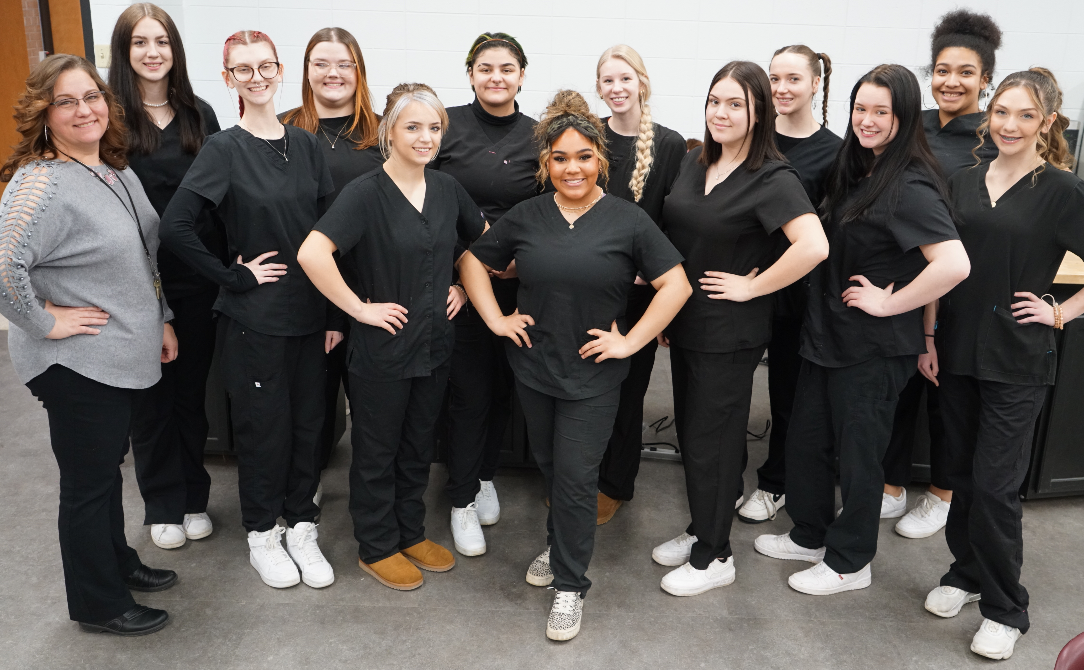 advanced  cosmetology class students standing with their hands on their hips in black scrubs