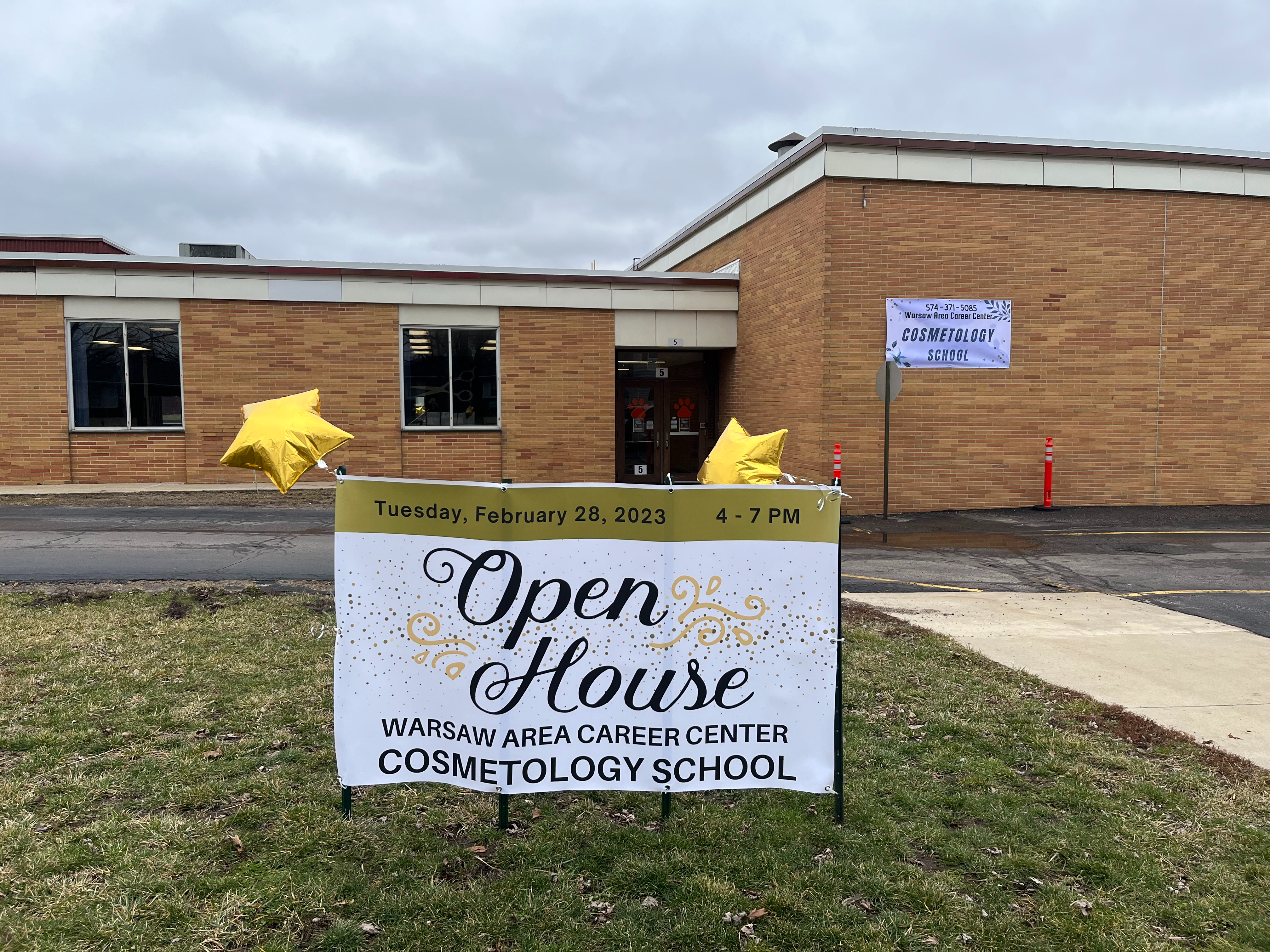 Open house banner for the warsaw area career center cosmetology school Tuesday, February 28th 2023 from 4-7pm. Banner is in the grass outside of the school entrance