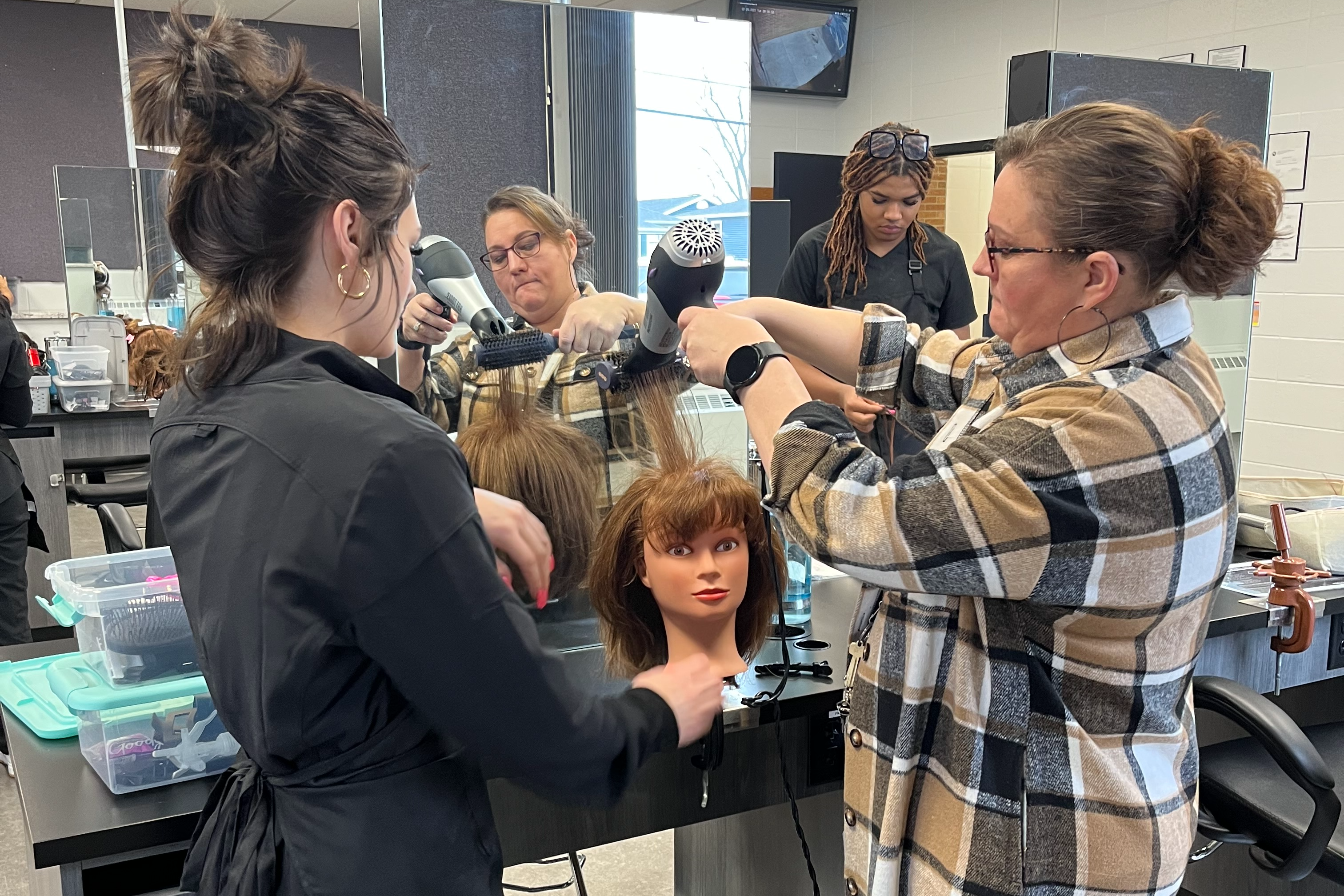 grace practices styling on a mannequin head under her teacher's guidance