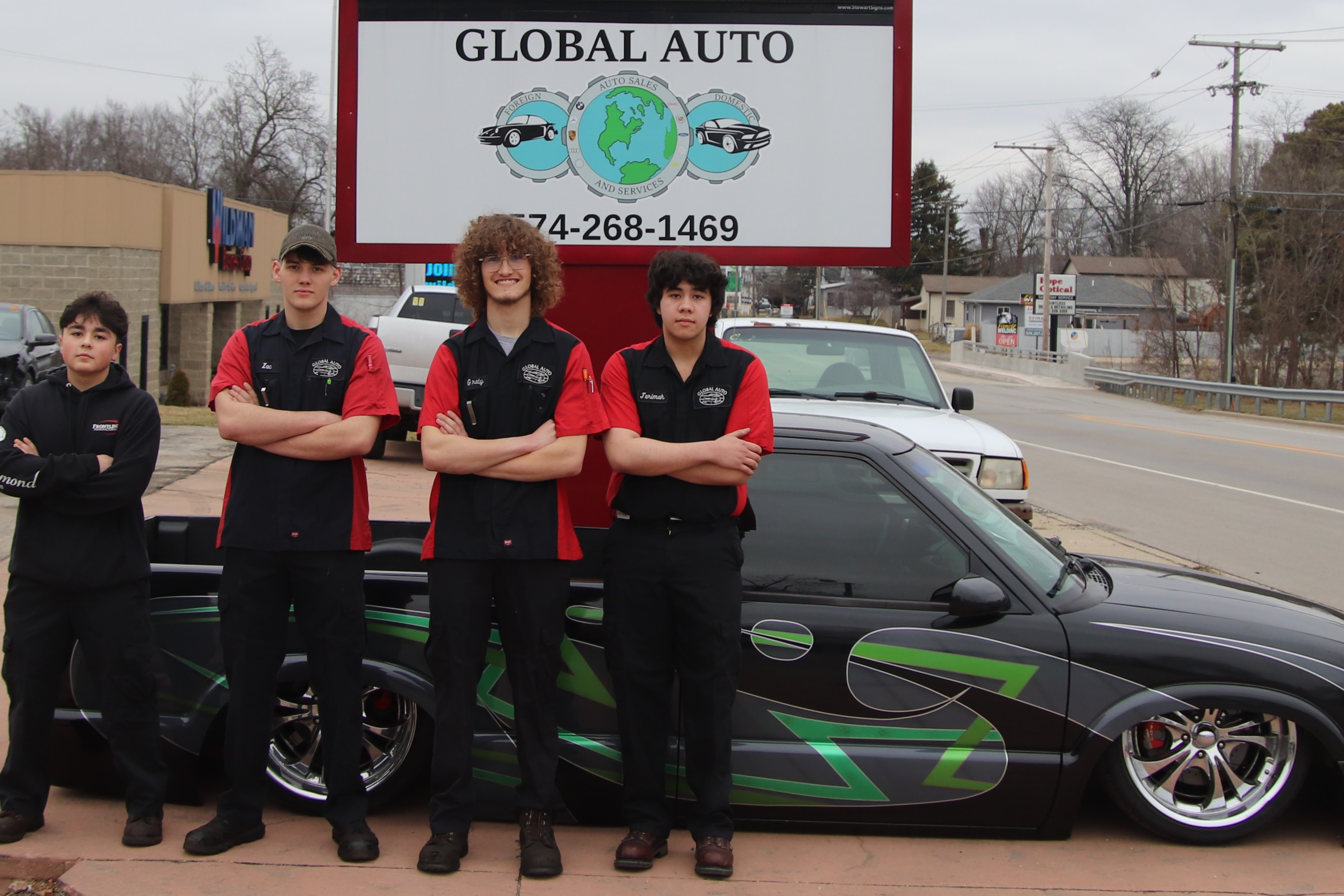 students posing with a sports car under global auto sign