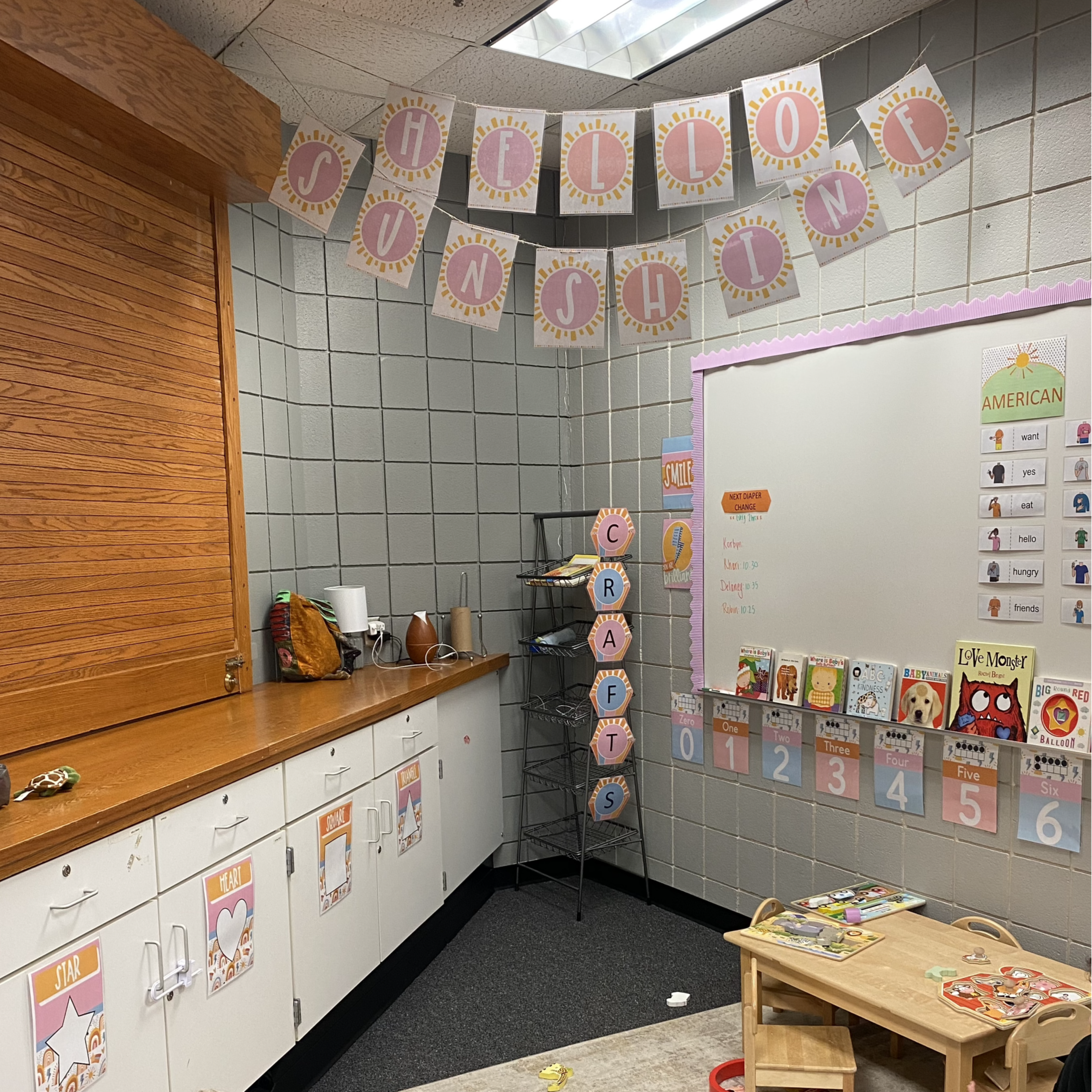 toddler classroom with "hello sunshine" banner across the ceiling and books and numbers set up on the white board