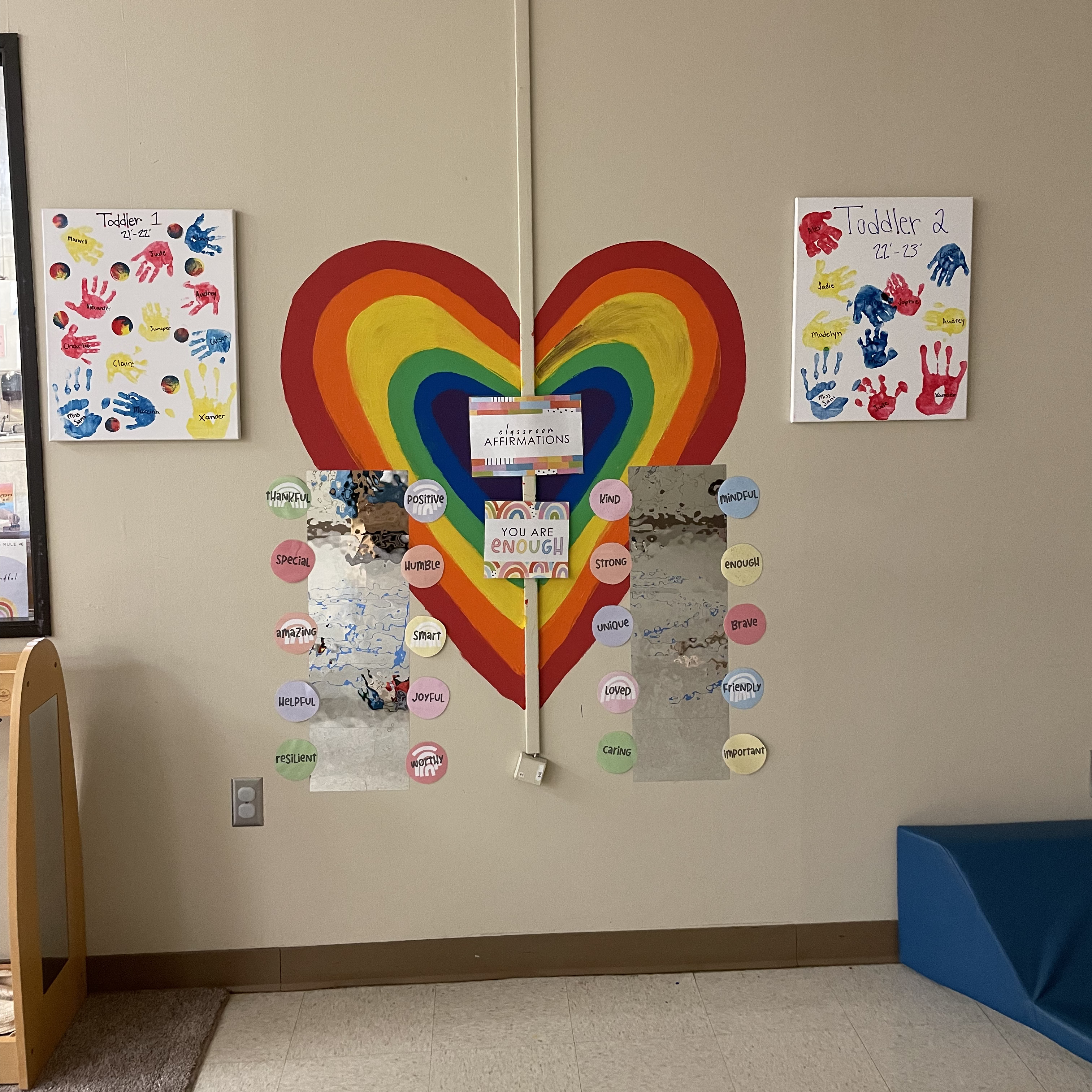 artwork with handprints and rainbow hearts displayed on the wall
