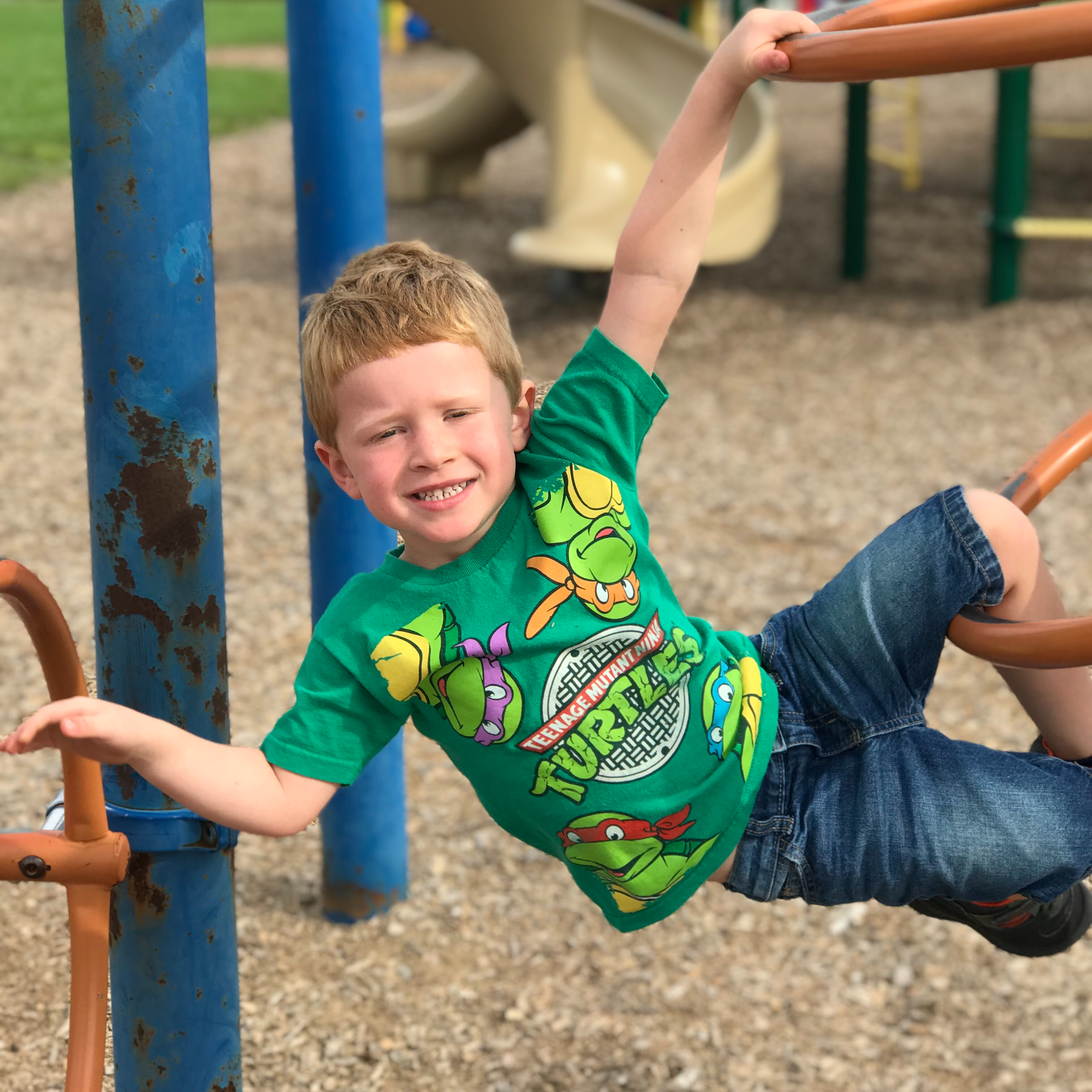 child hanging from playground equipment and smiling