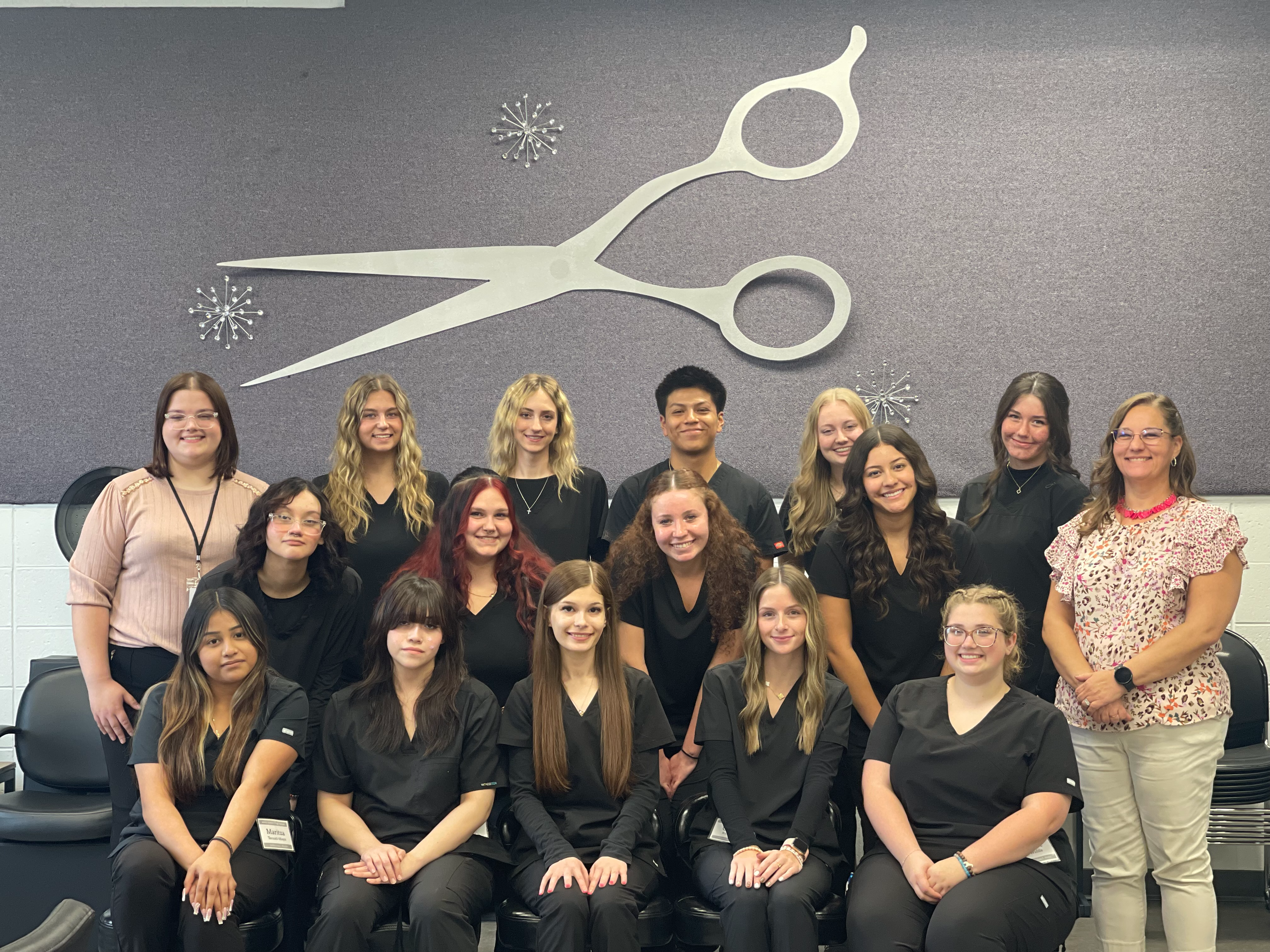 advanced  cosmetology class students standing with their hands on their hips in black scrubs