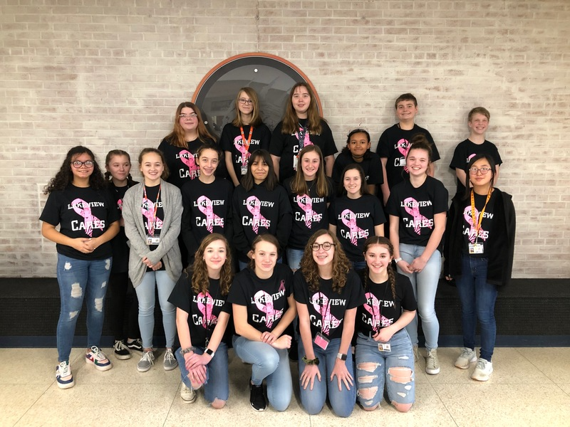 a group of students wearing "Lakeview Cares" shirts with pink breast cancer ribbons pose in front of a brick wall