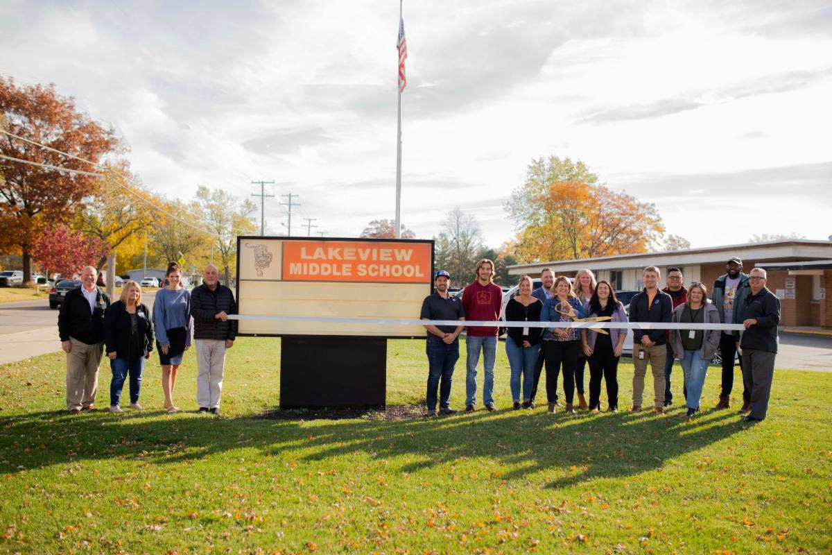 A group of staff and students pose next to the lakeview middle school marquee sign and host a ribbon cutting ceremony