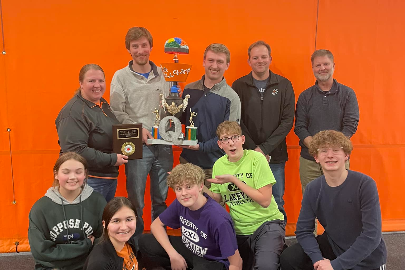 Quiz bowl team posing with their trophy against an orange background