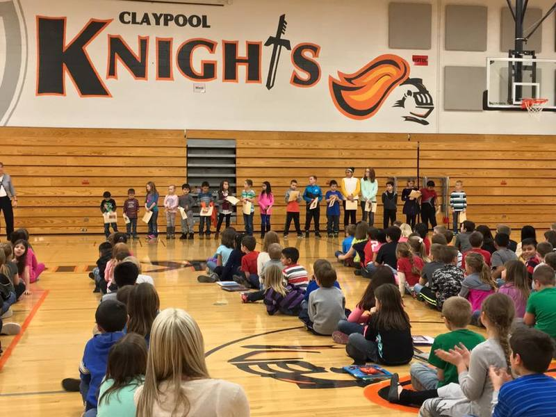 Students seated in the gym with a line of students standing under the claypool knights wall mural