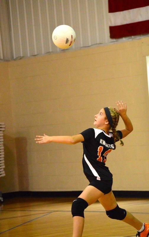 A volleyball player in uniform prepares to hit the ball as it approaches from above