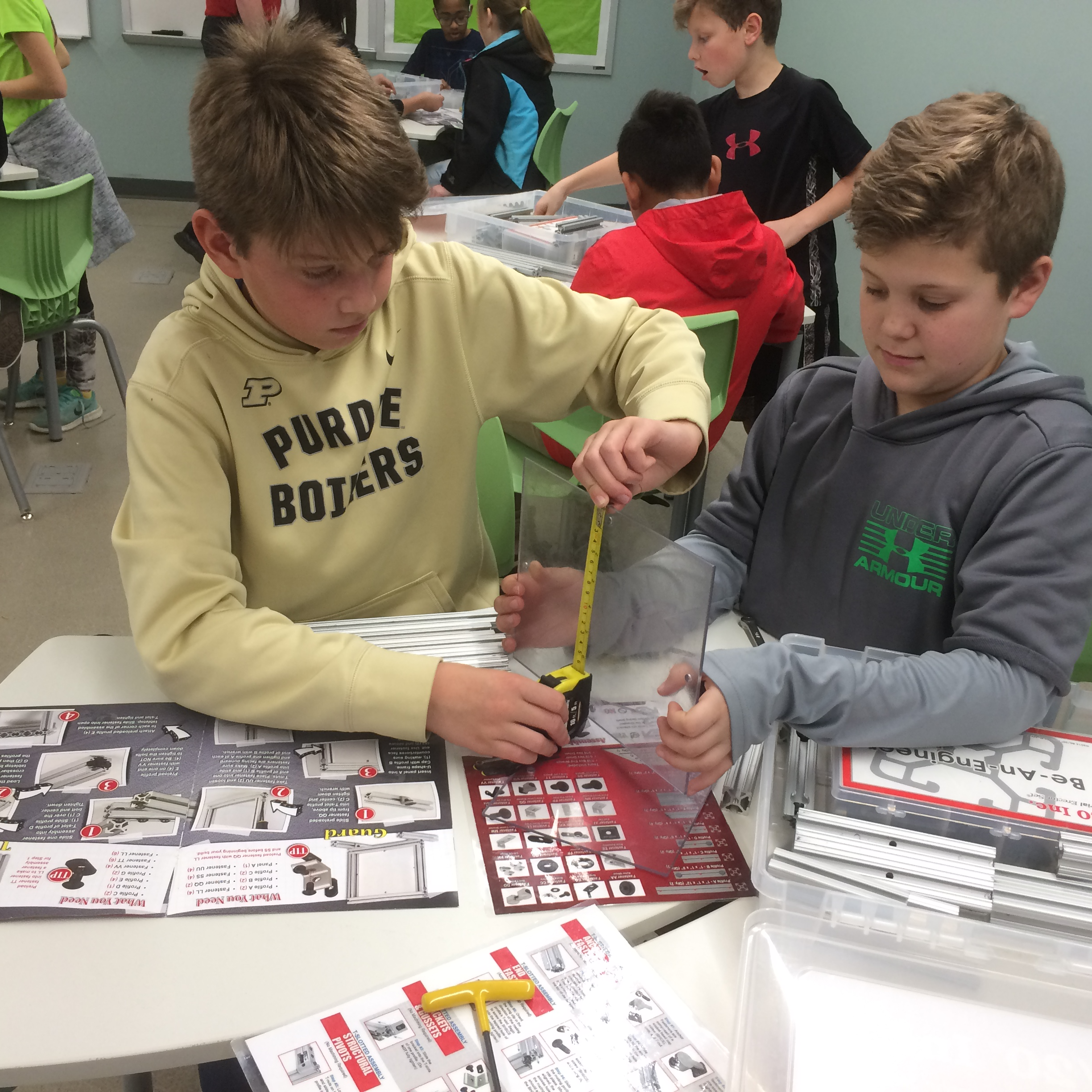 Students with tape measurer measuring out a sheet of glass