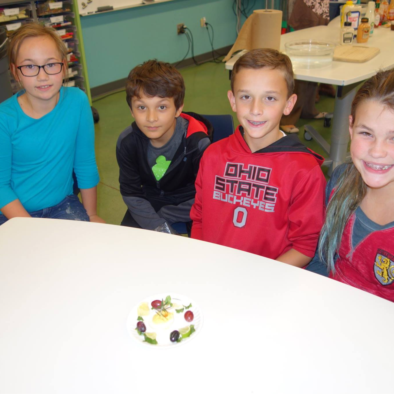 Students at a table with a few fruits and vegetables on a plate