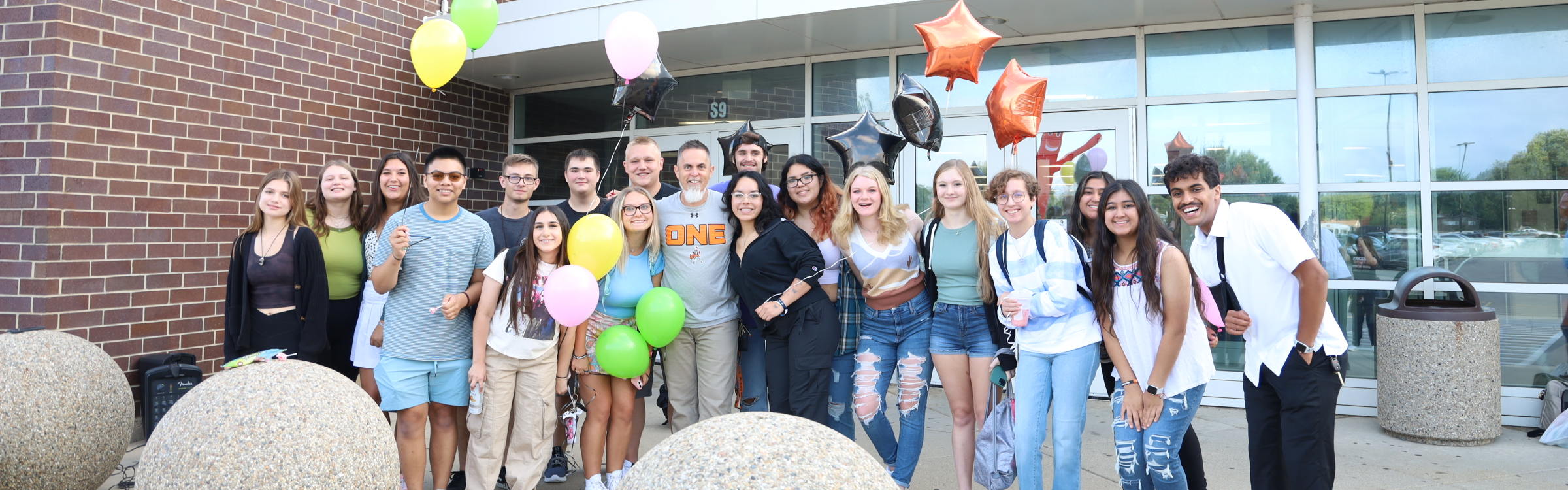 Students posing in front of the student entrance with balloons on the first day of school