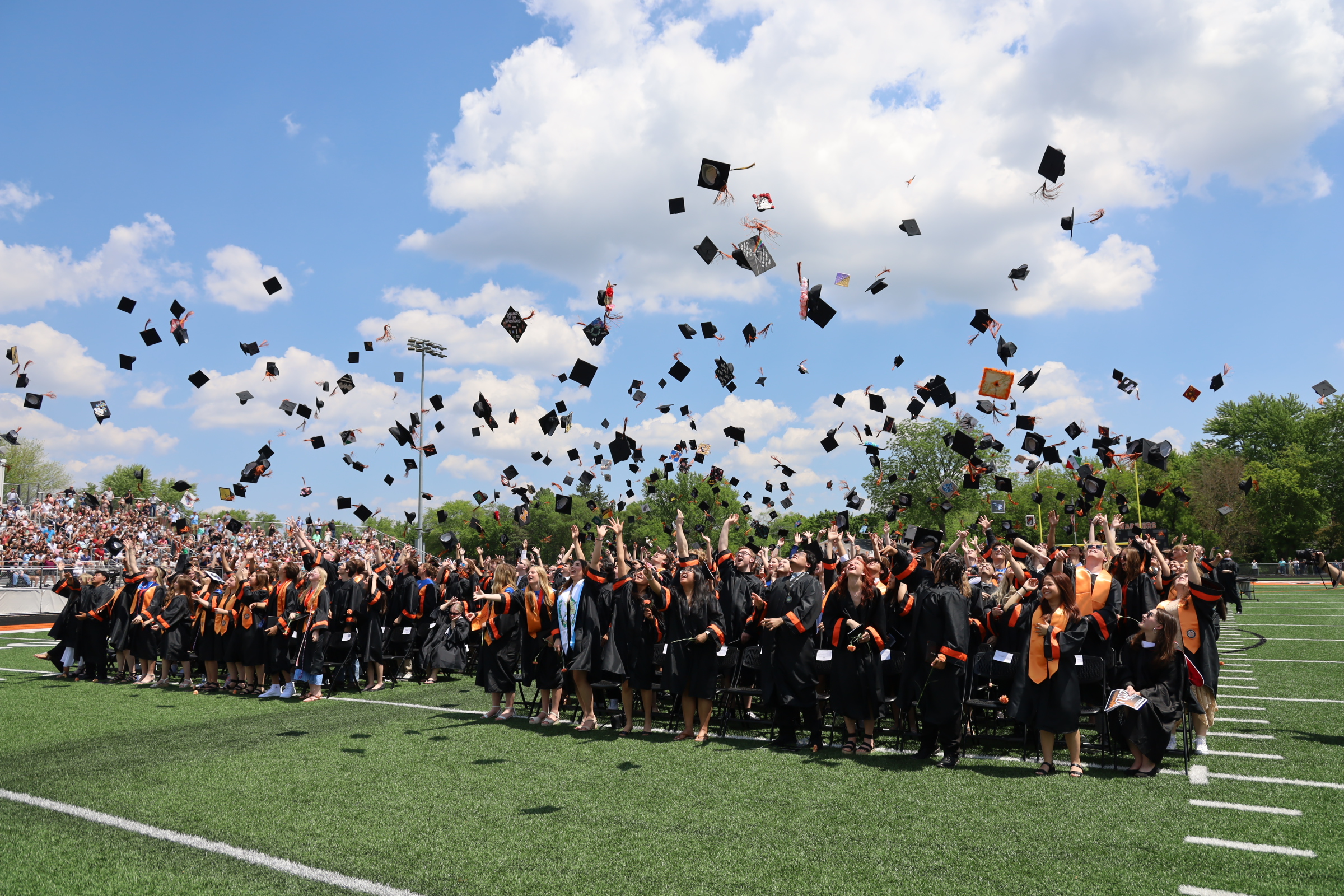 Seniors throwing graduation hats at football field